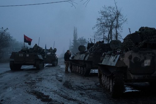 Ukrainian service member smokes next to armoured personnel carriers on a road in Kherson region