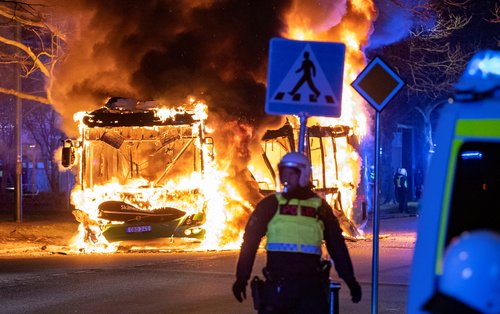 A police personnel stands near a burning bus after a demonstration organised by Rasmus Paludan turned violent, in Malmo