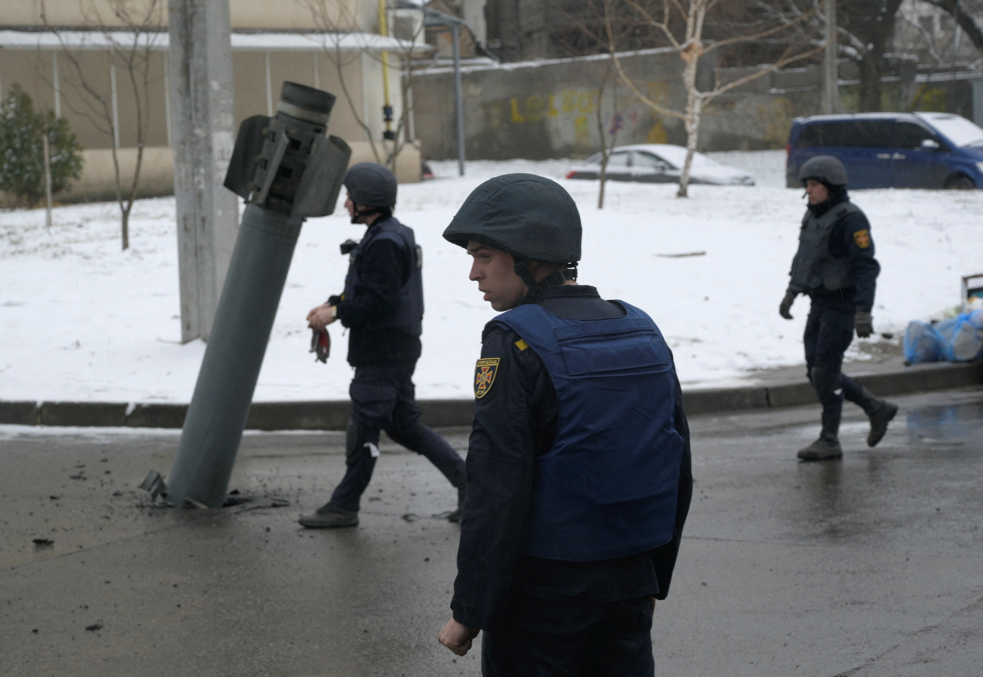 Rescuers walk towards a rocket case stuck on the driveway following recent shelling in Kharkiv