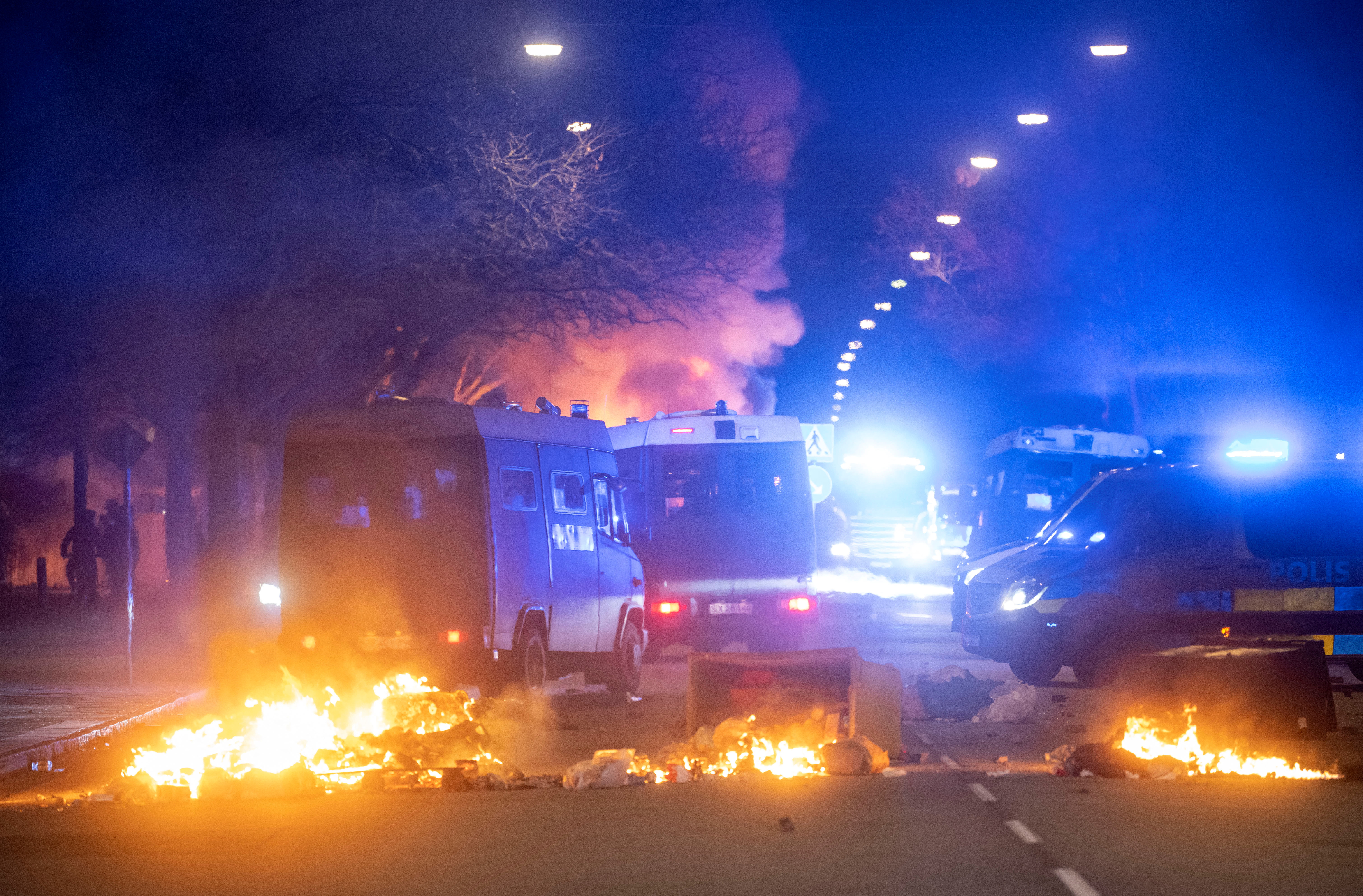 Police riot control vans are seen near burning garbage cans after a demonstration organised by Rasmus Paludan turned violent, in Malmo