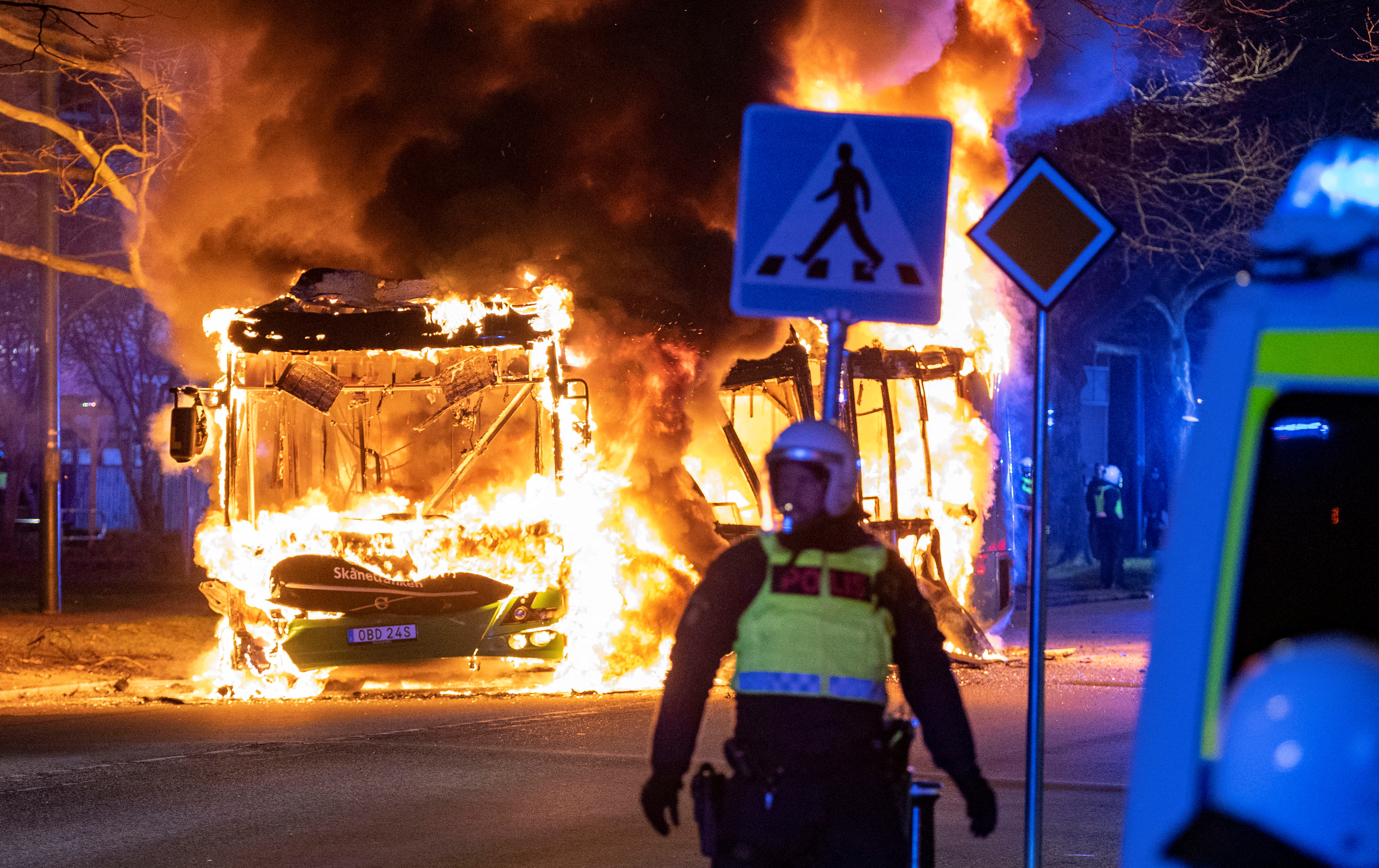 A police personnel stands near a burning bus after a demonstration organised by Rasmus Paludan turned violent, in Malmo