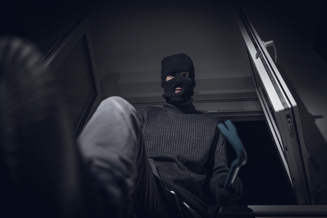 Bavaria, Germany - 07 October 2022: Masked Burglar Pries Open A Window With Crowbar And Breaks Into A House At Night