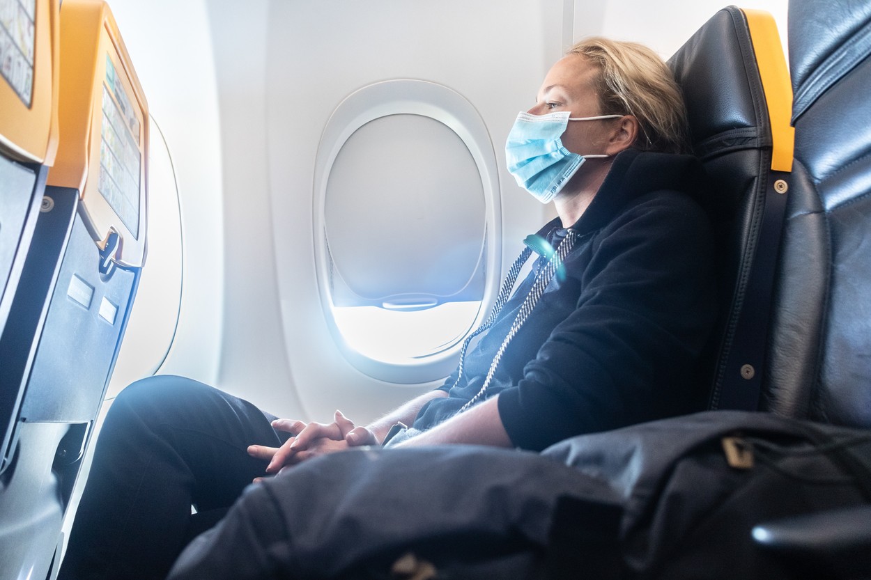 A young woman wearing face mask is traveling on airplane , New normal travel after covid-19 pandemic concept.