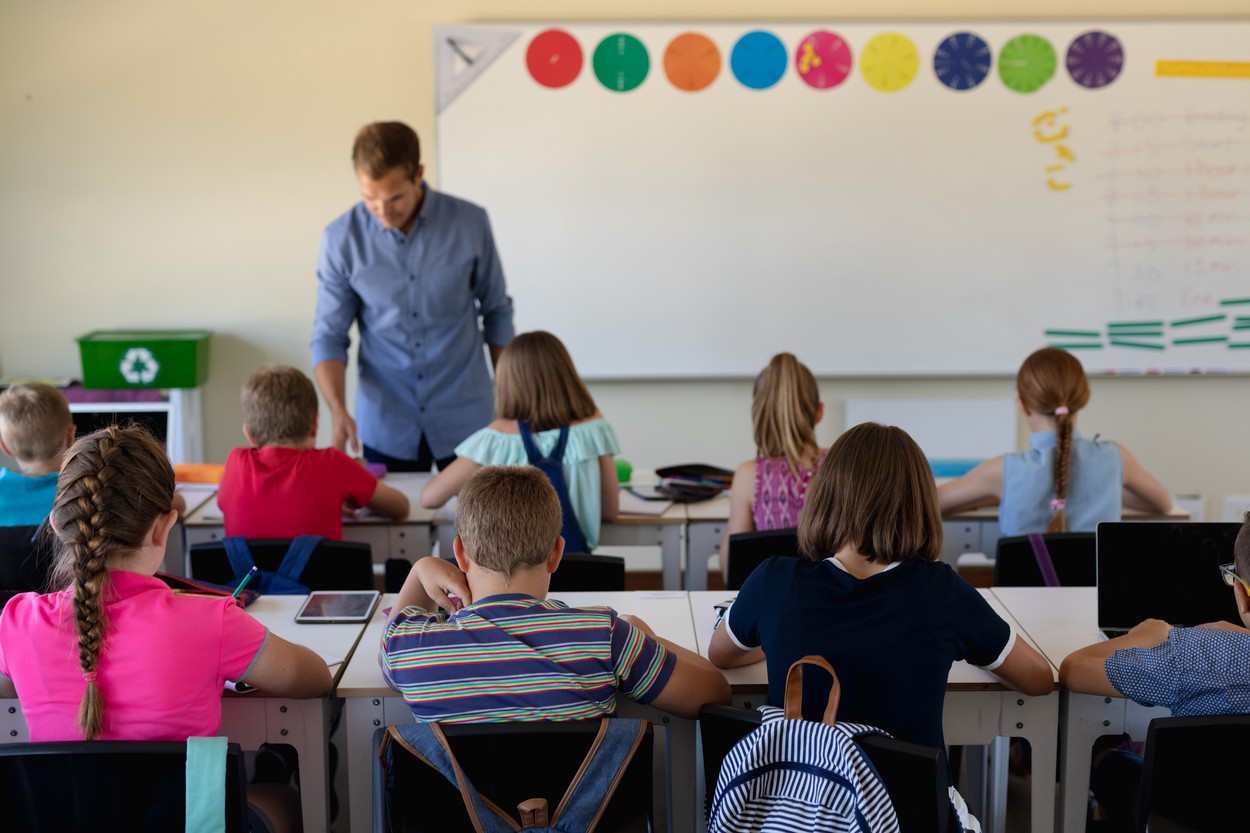 Male school teacher standing in an elementary school classroom with a group of school children