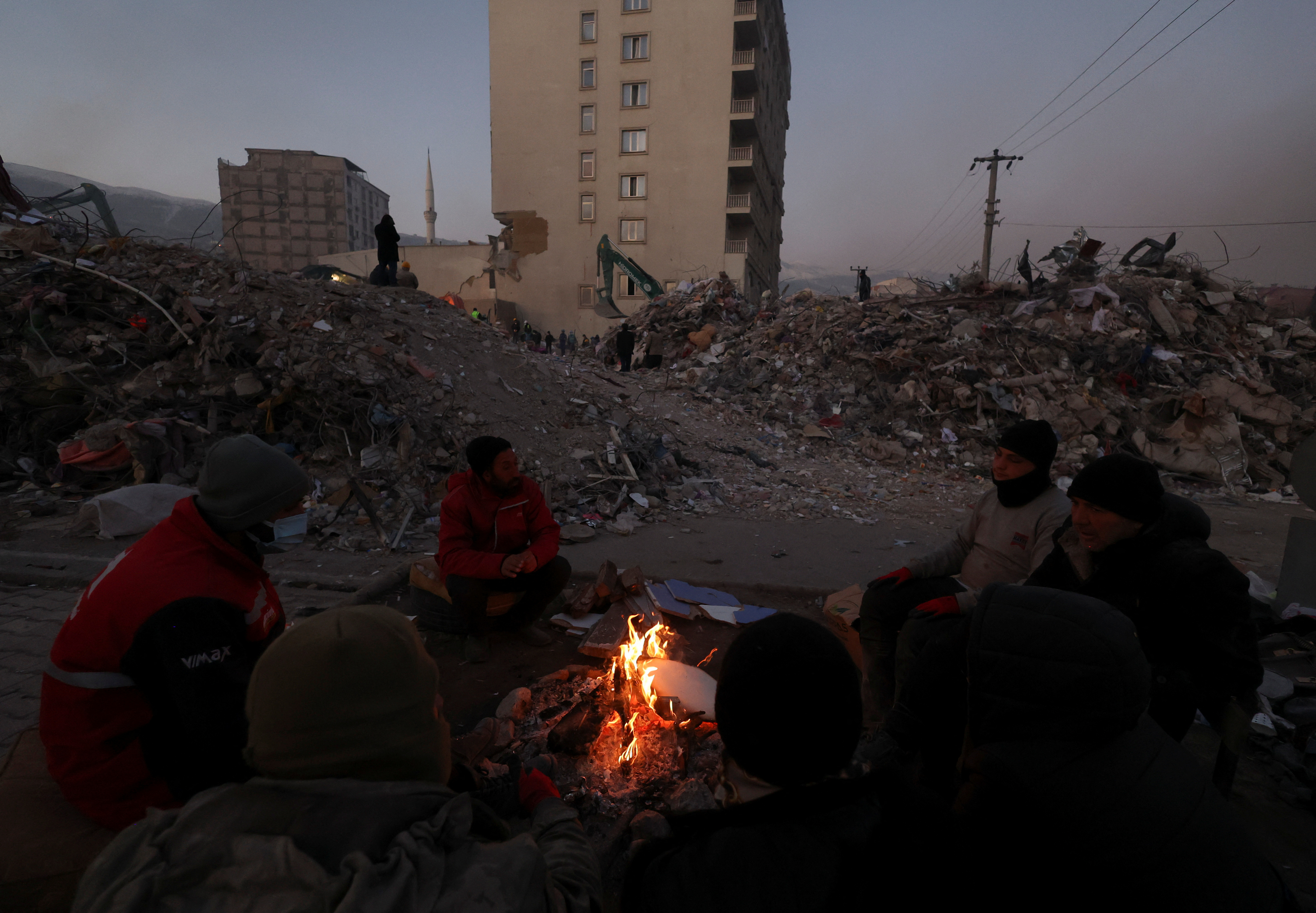 posledice potresa v Turčiji, ruševine, ljudje sedijo ob ognju