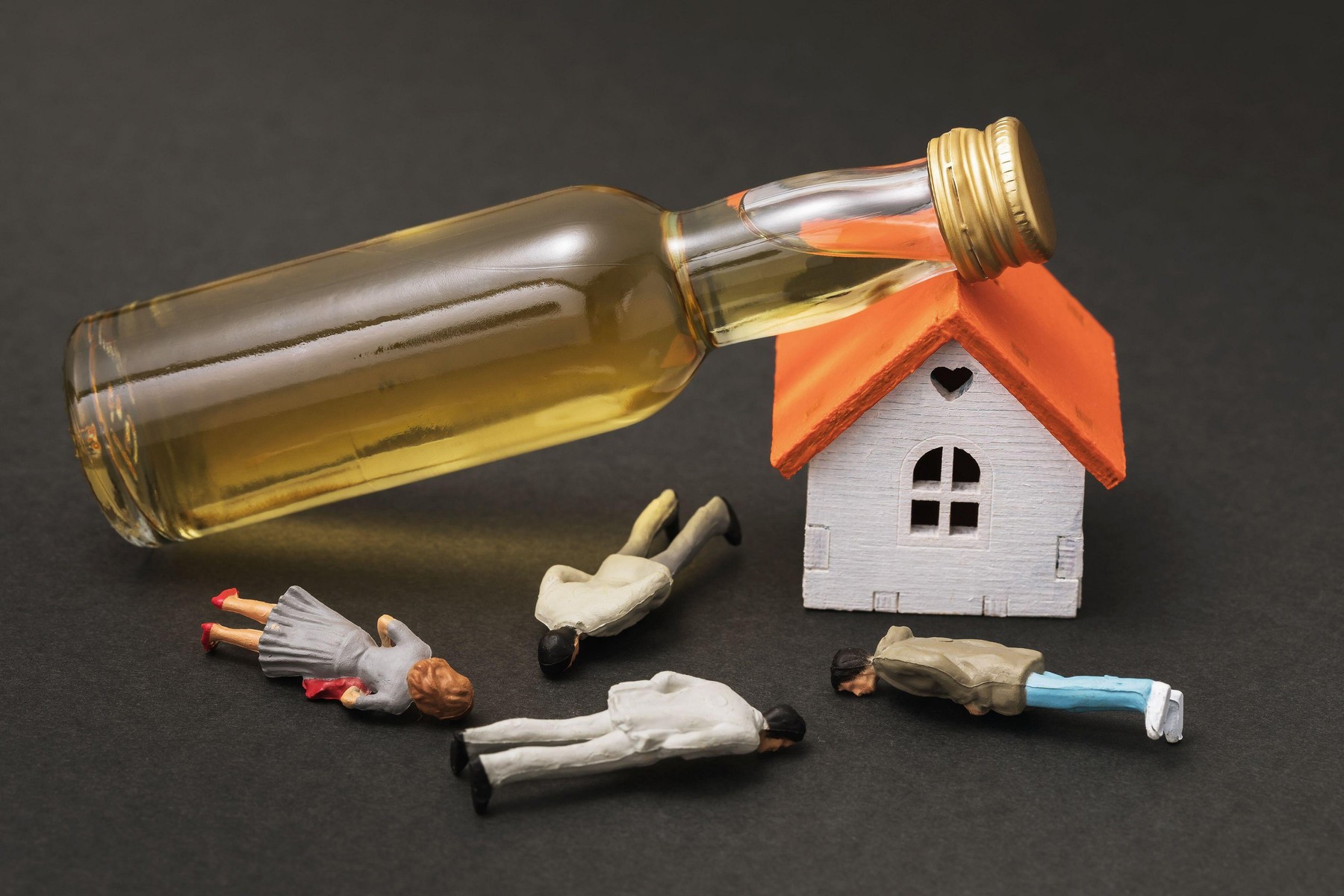 Toy men made of plastic, a small house and a bottle of whiskey on a dark background, a concept on the topic of alcohol abuse