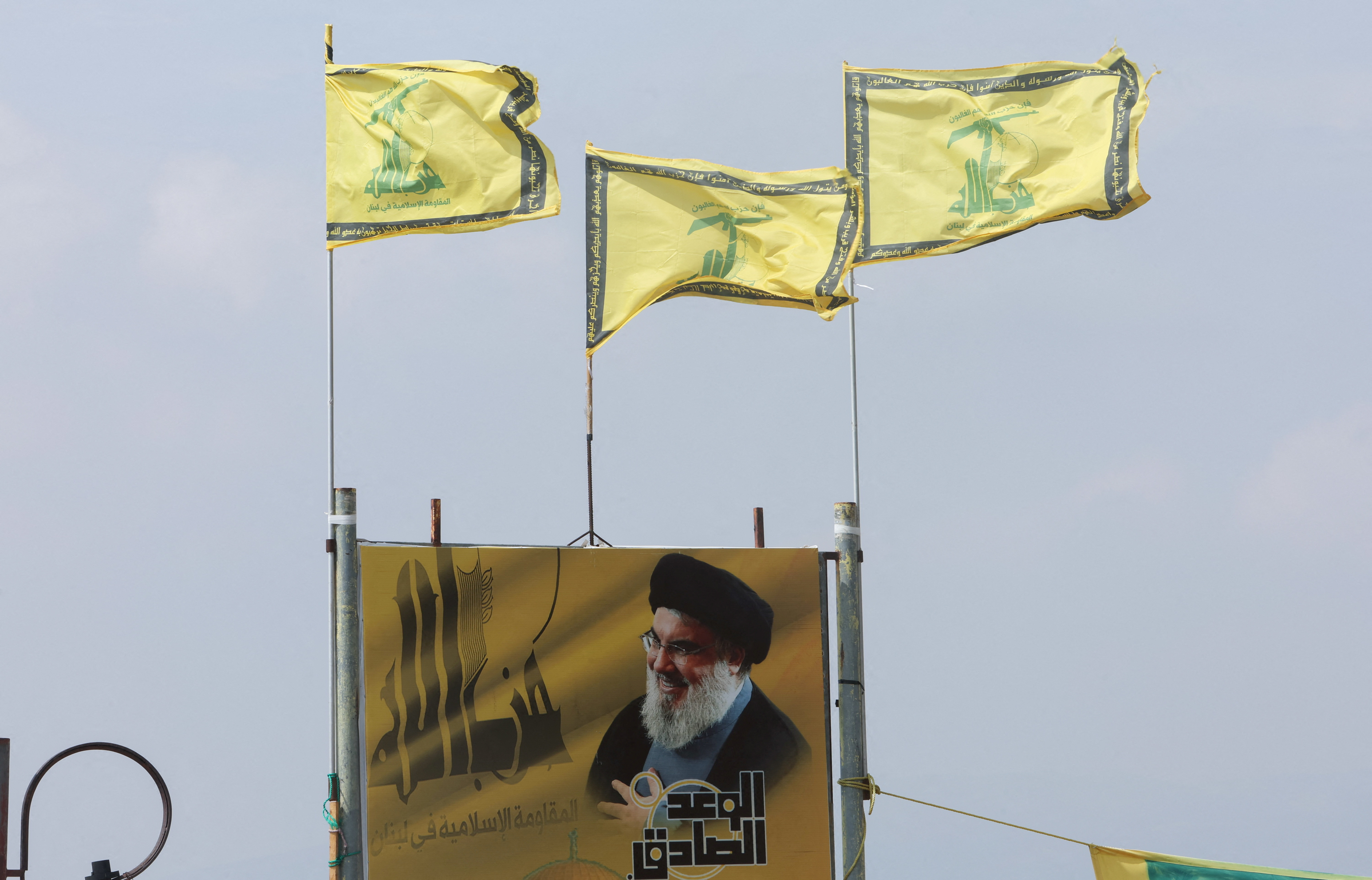 Hezbollah flags flutter atop a poster depicting Lebanon's Hezbollah leader Sayyed Hassan Nasrallah, in Kfarchouba