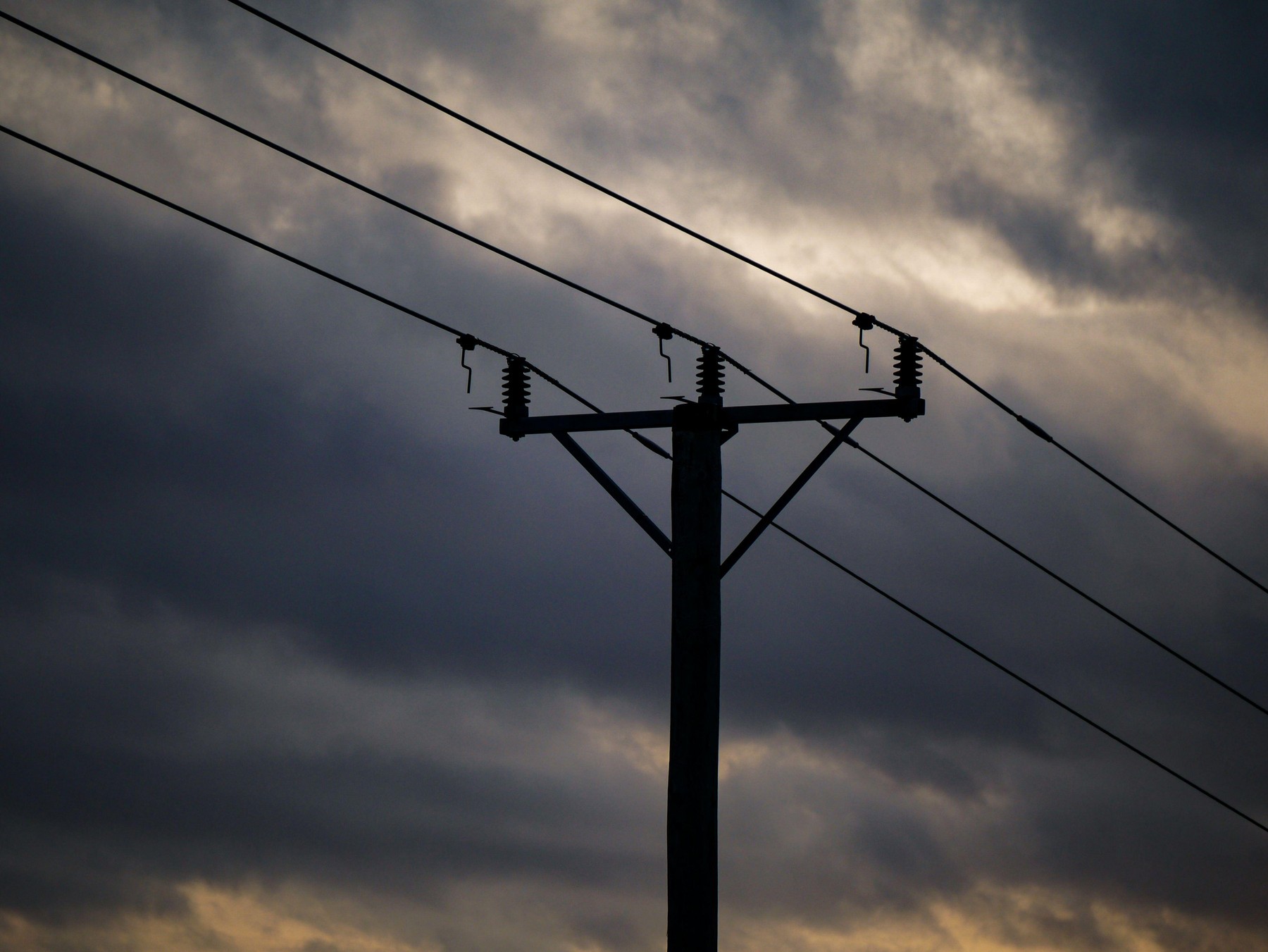 Low angle view of silhouette electricity pylon against cloudy sky