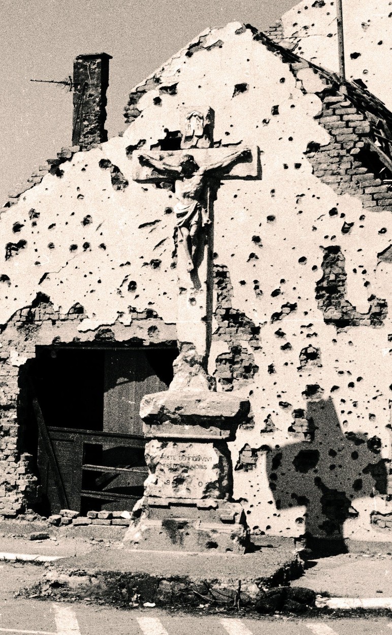 A crucifix of Jesus Christ is pockmarked by bullets and bombs on a street corner in Vukovar, Croatia, on Thursday, November 21, 1991.
