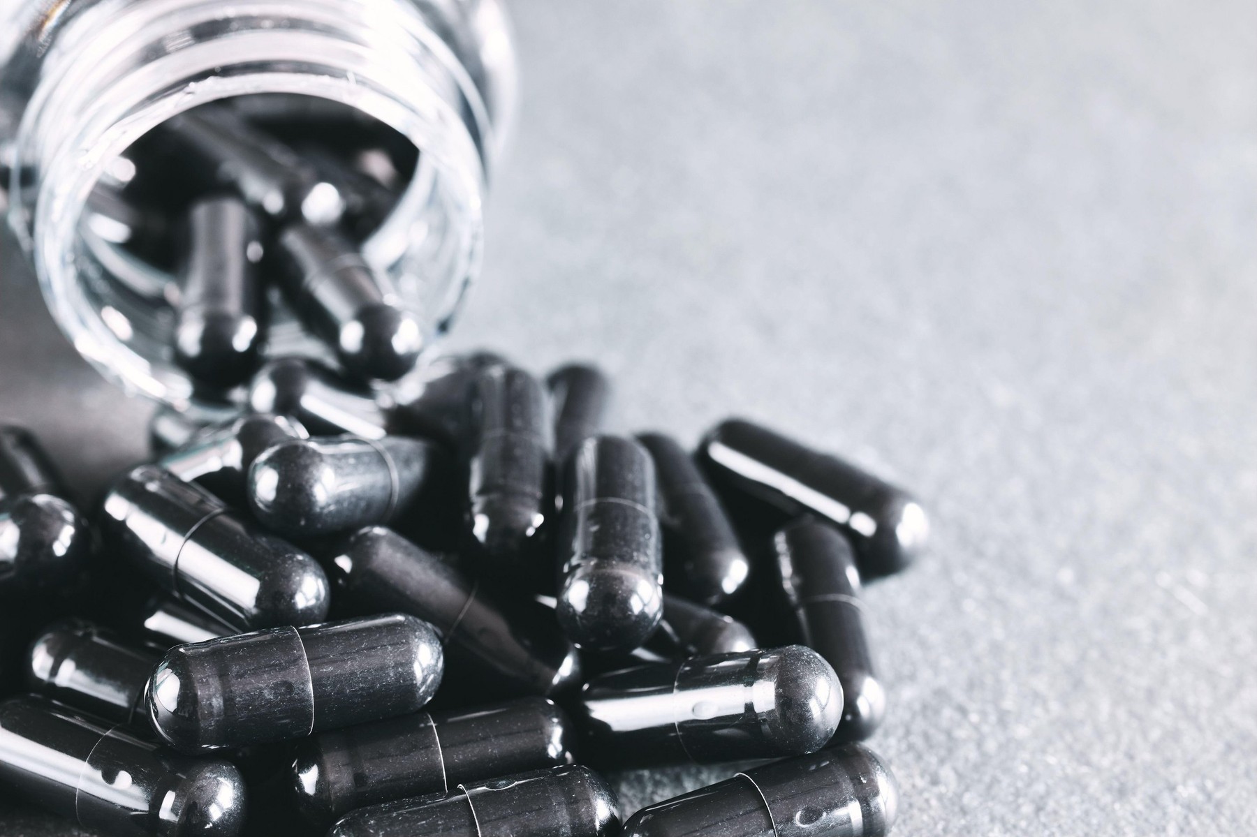 Close up picture of black capsules spill out of container, selective focus, color toning applied.