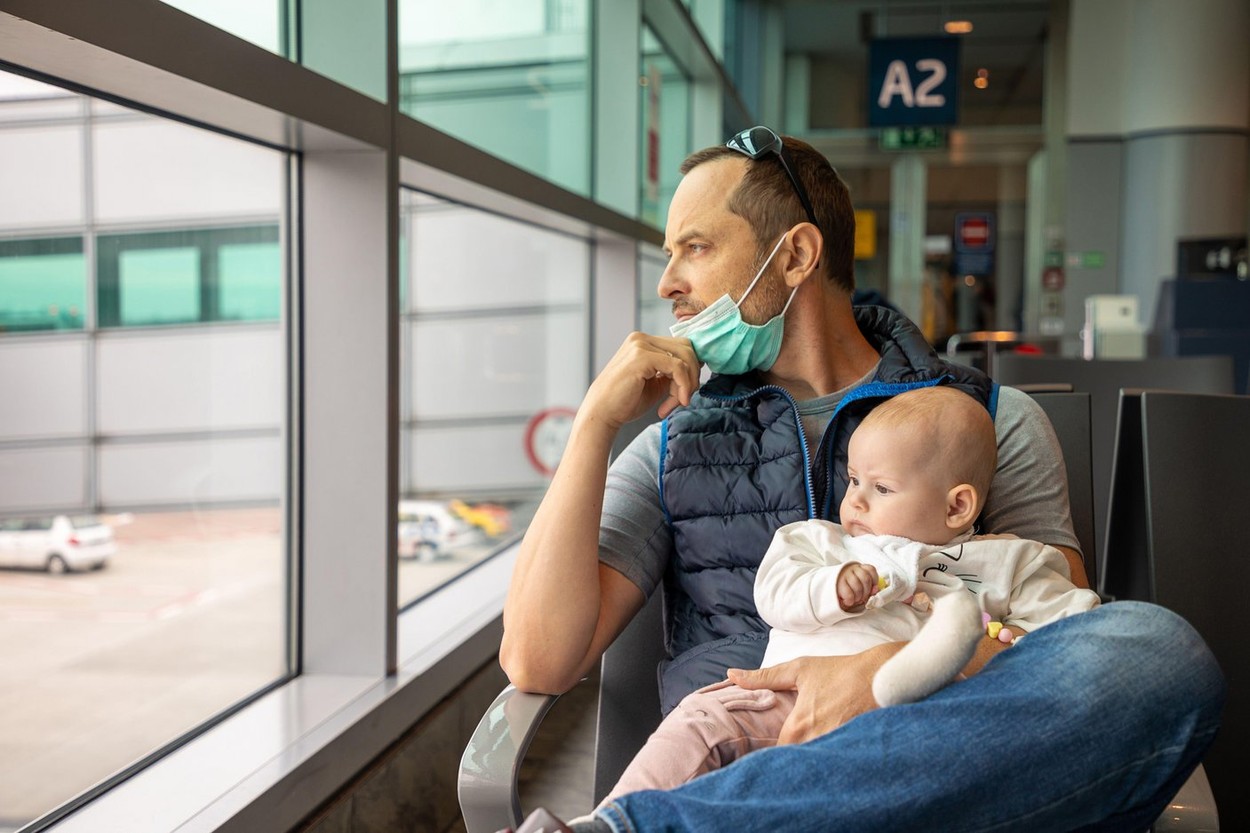 Father in medical mask and his daughter small baby girl waiting a boarding on plane at the airport in Prague, Czech republic