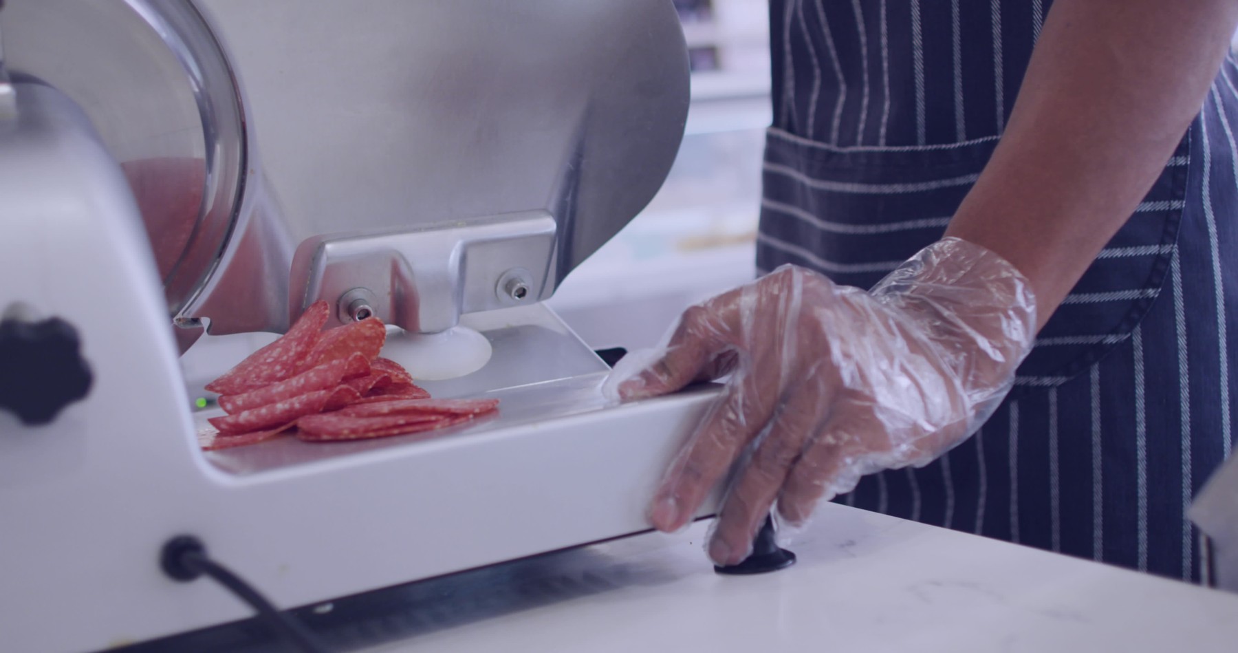 Person slices salami on a meat slicer at a deli