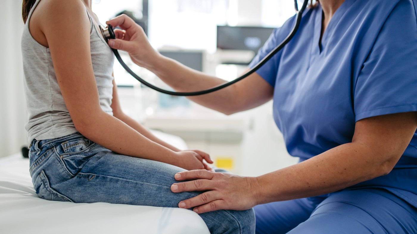 Doctor examining young girl, listening to heartbeat, breathing, using stethoscope. School entry medical exam. Female Doc