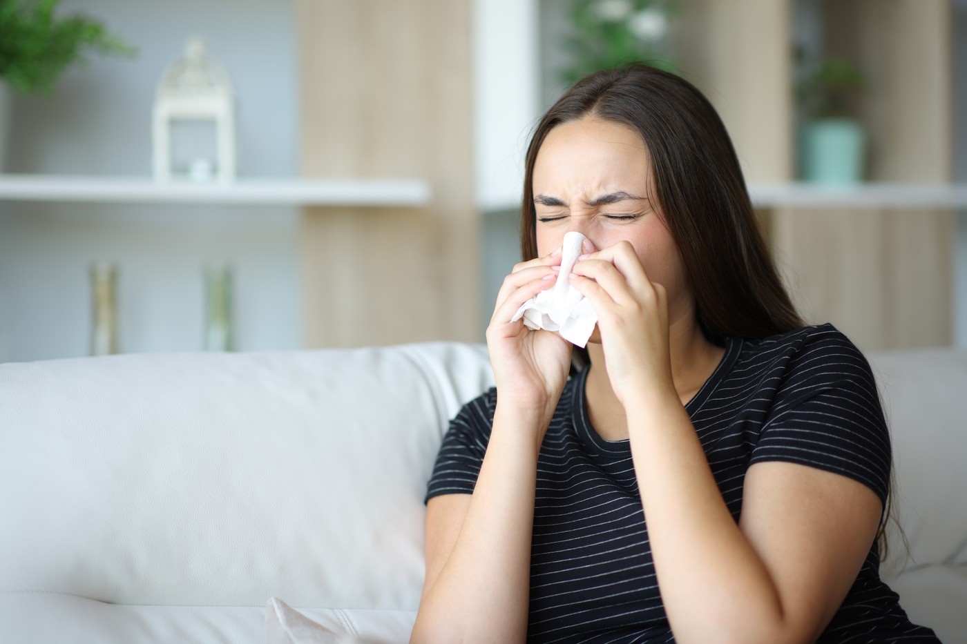 Ill woman sneezing using tissue at home