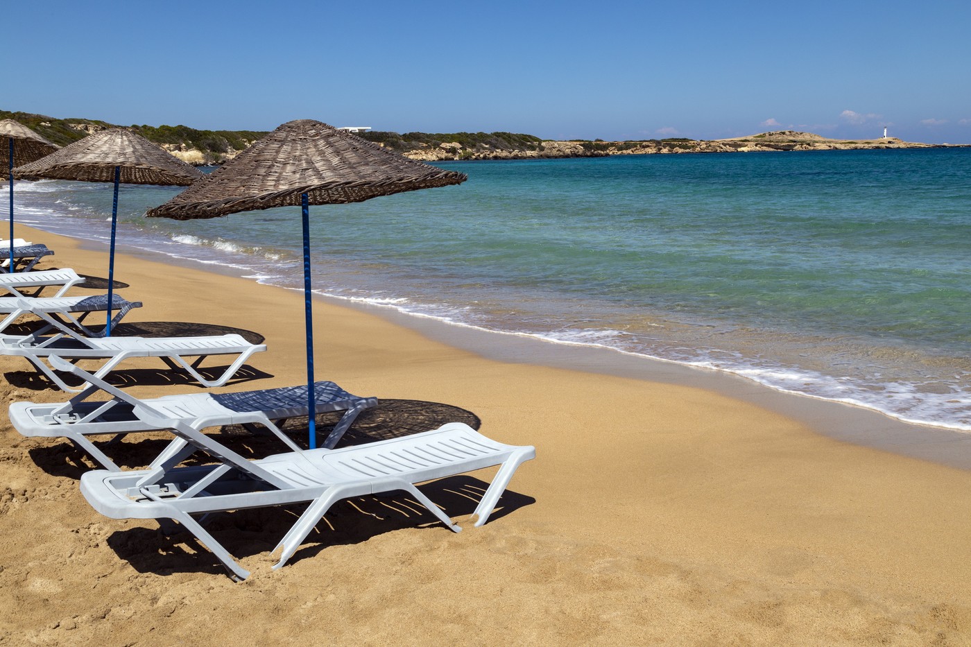 Ležalniki na peščeni plaži ob morju.