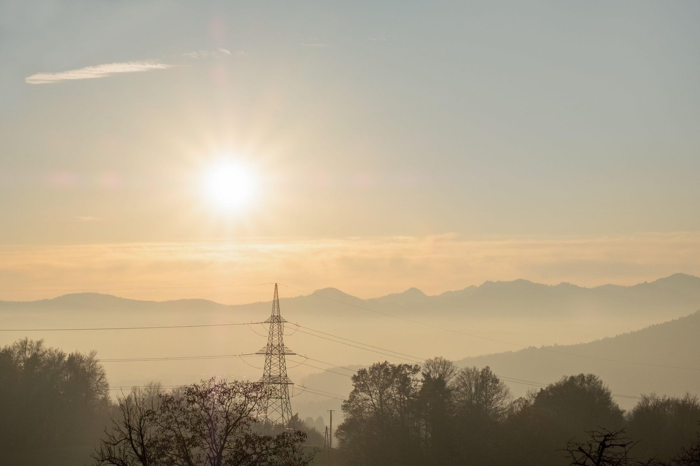 view of electricity infrastructure, power pole and cables set in a beautiful landscape scenery with misty mountains and the setting sun.