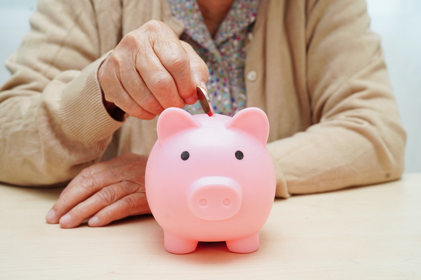 Retired elderly woman putting coins money in piggy bank and worr