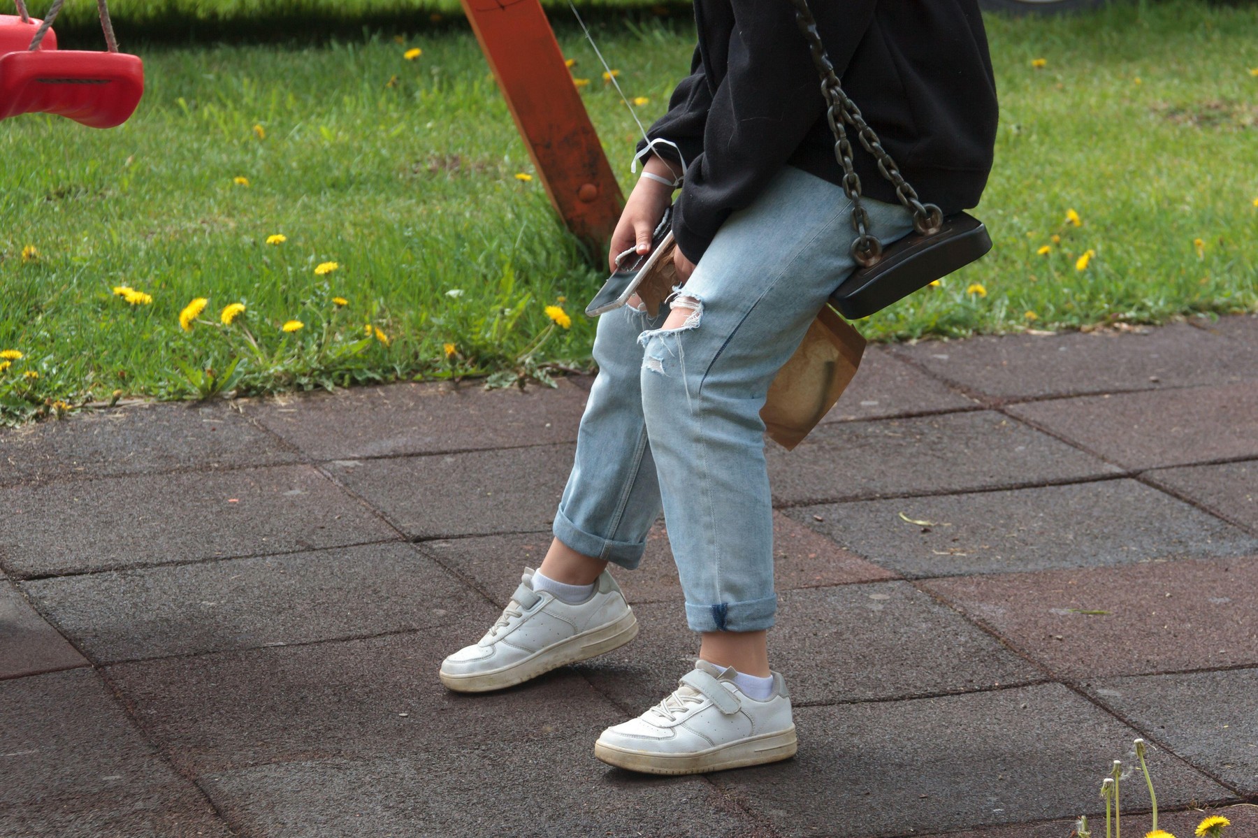 legs of a teenager sitting on a swing at the playground alone