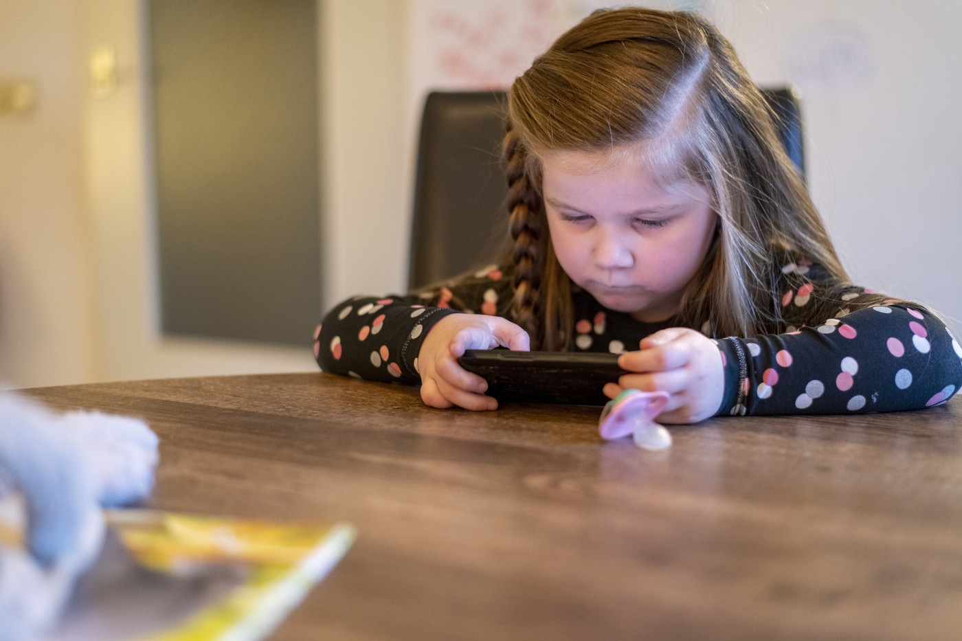 Young girl sitting at her family dining room table playing on her mothers phone. concentrating trying to win