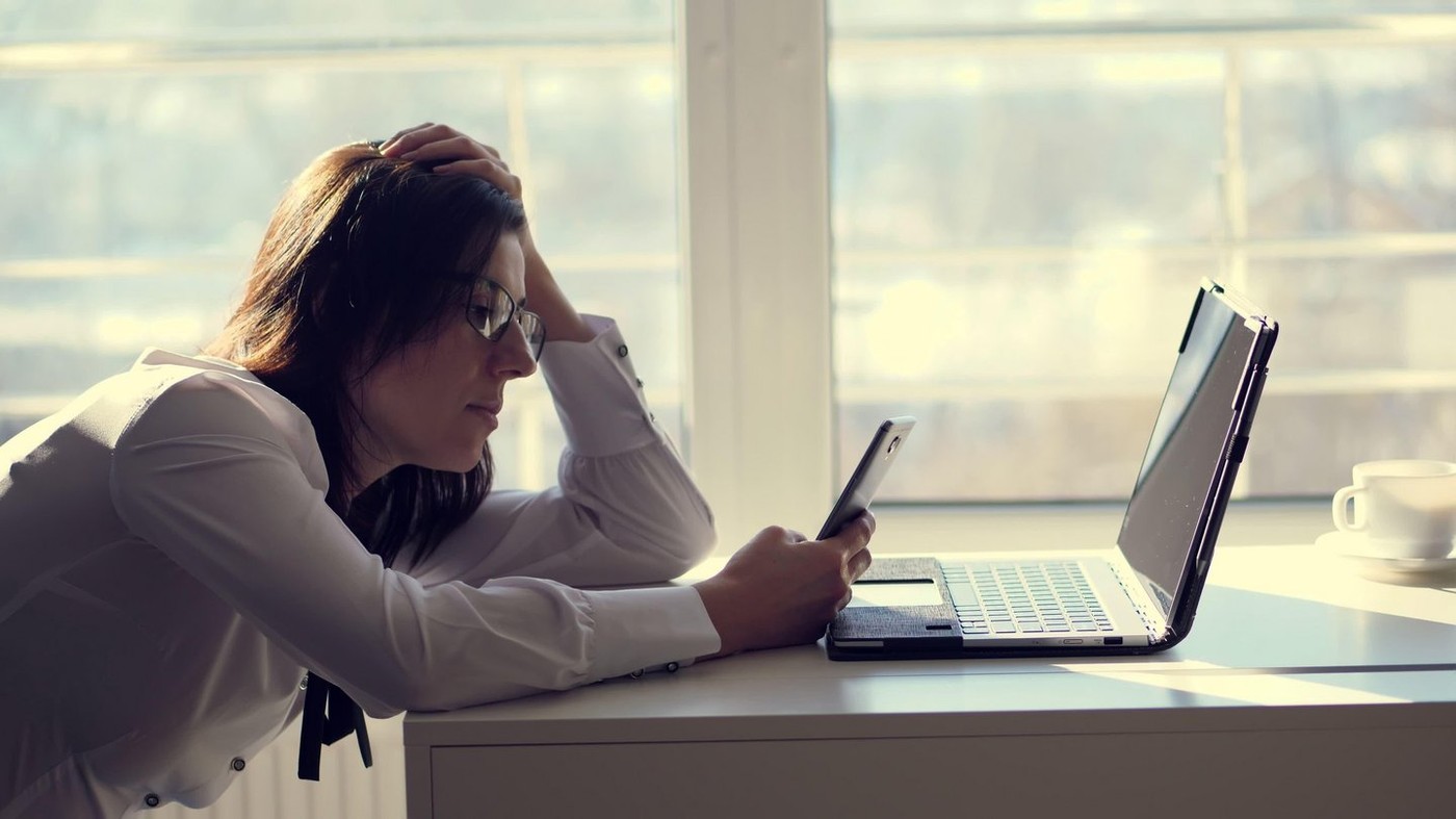 A young female clerk office worker browses social networks on a mobile phone, during her work day, in an office. a short break, rest in work. possible concept of unscrupulous and lazy employee or tired. High quality photo