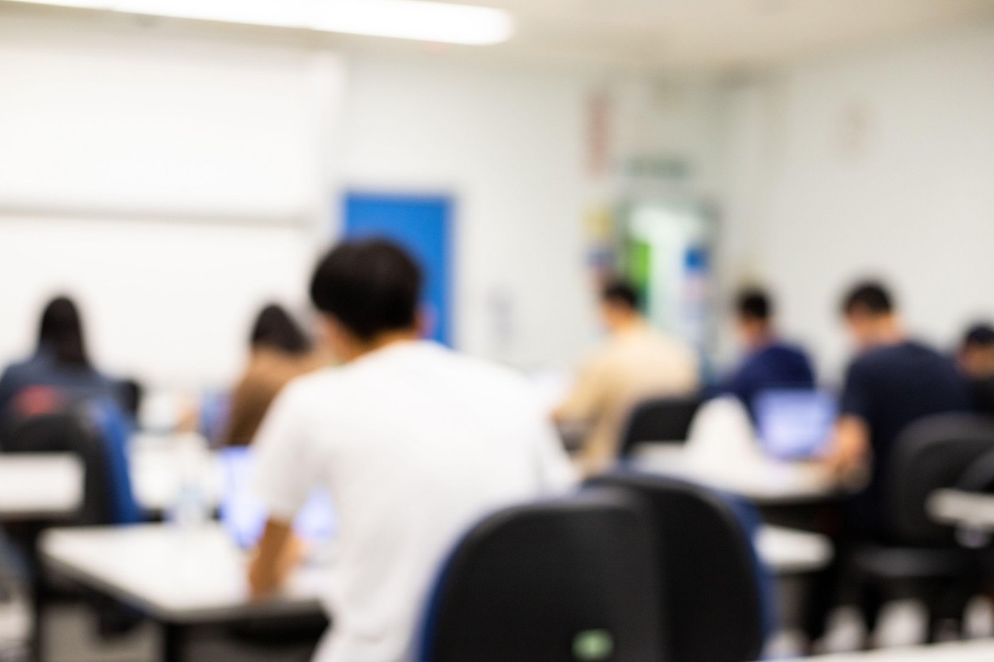 blurred classroom university students sitting with computers in lecture hall, seminar or meeting / conference room with teacher, white board/slide scr