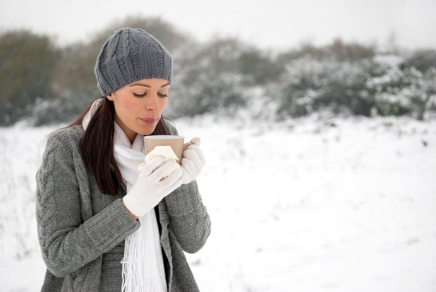 Woman with cold blowing on hot drink outside holding tissue