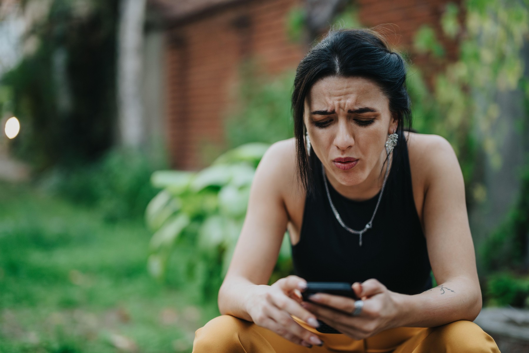 zaskrbljena ženska na vrtu z mobilnim telefonom