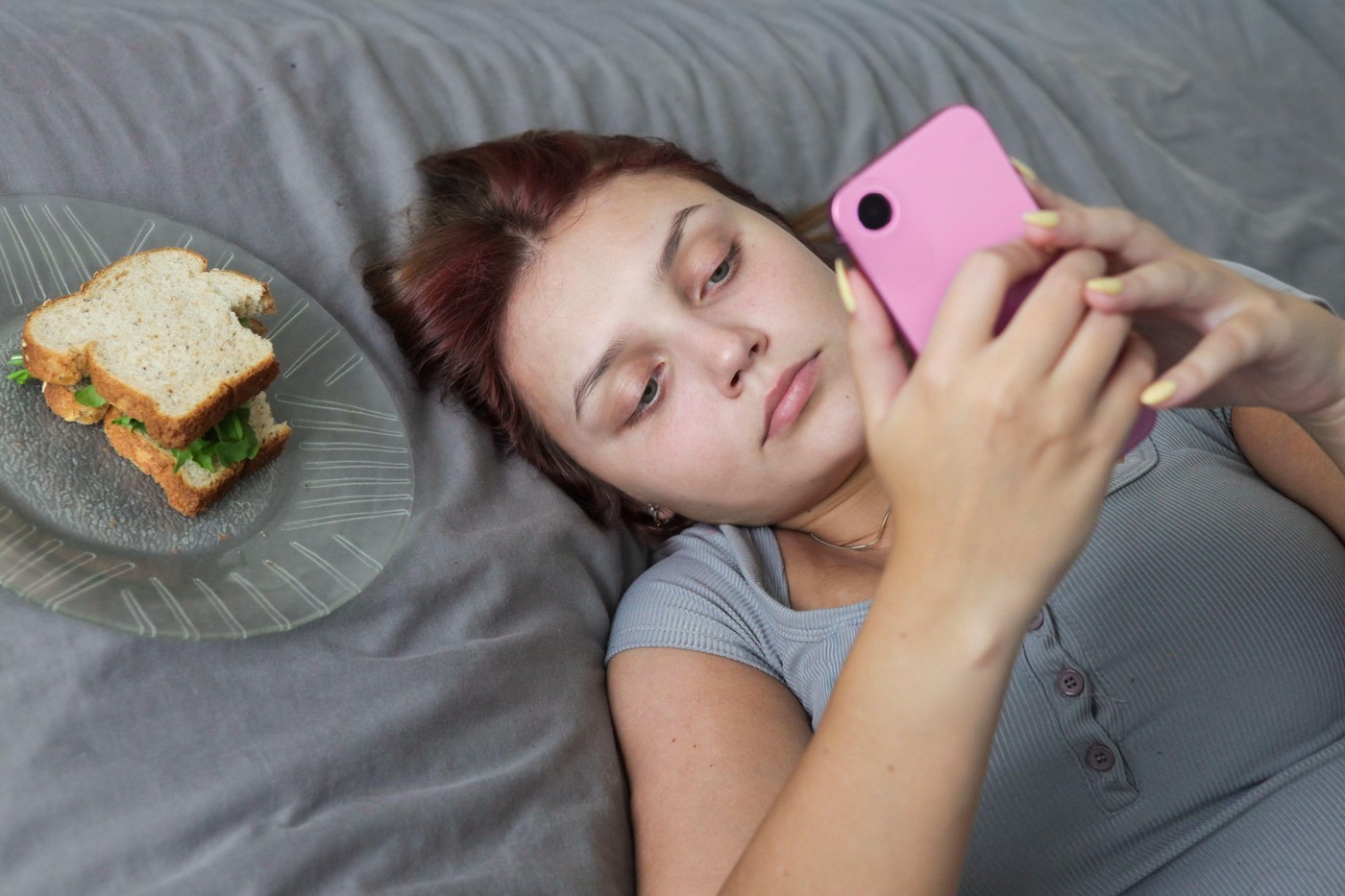 mlada ženska v postelji s telefonom in sendvičem