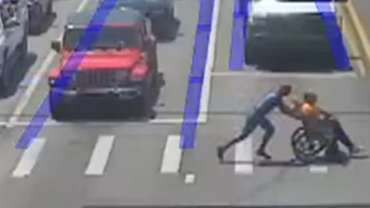 moški v Spidermanovem kostumu pomaga invalidu v vozičku preko ceste