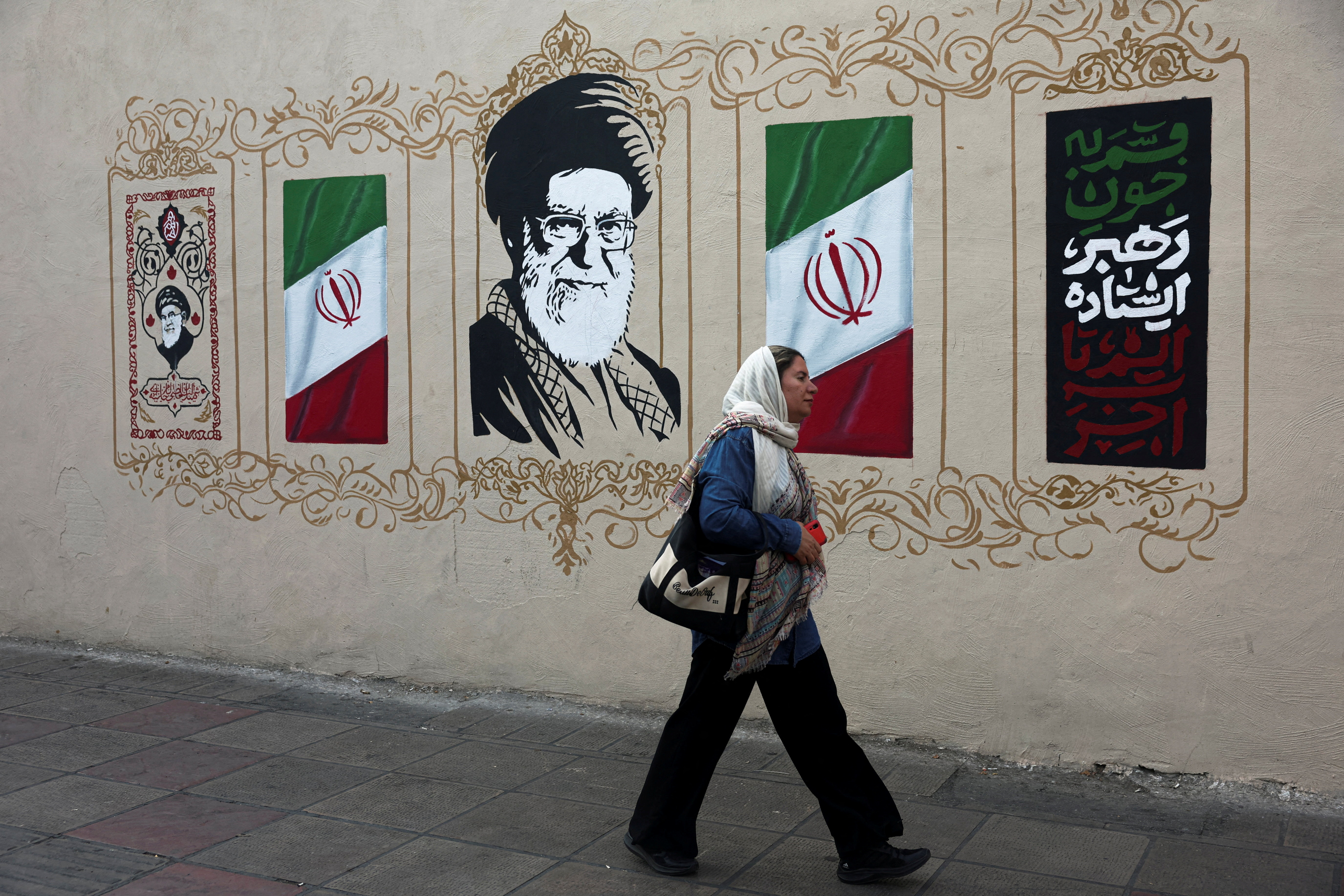 Iranka hodi mimo portreta pokojnega vrhovnega voditelja Alija Hameneja v Teheranu