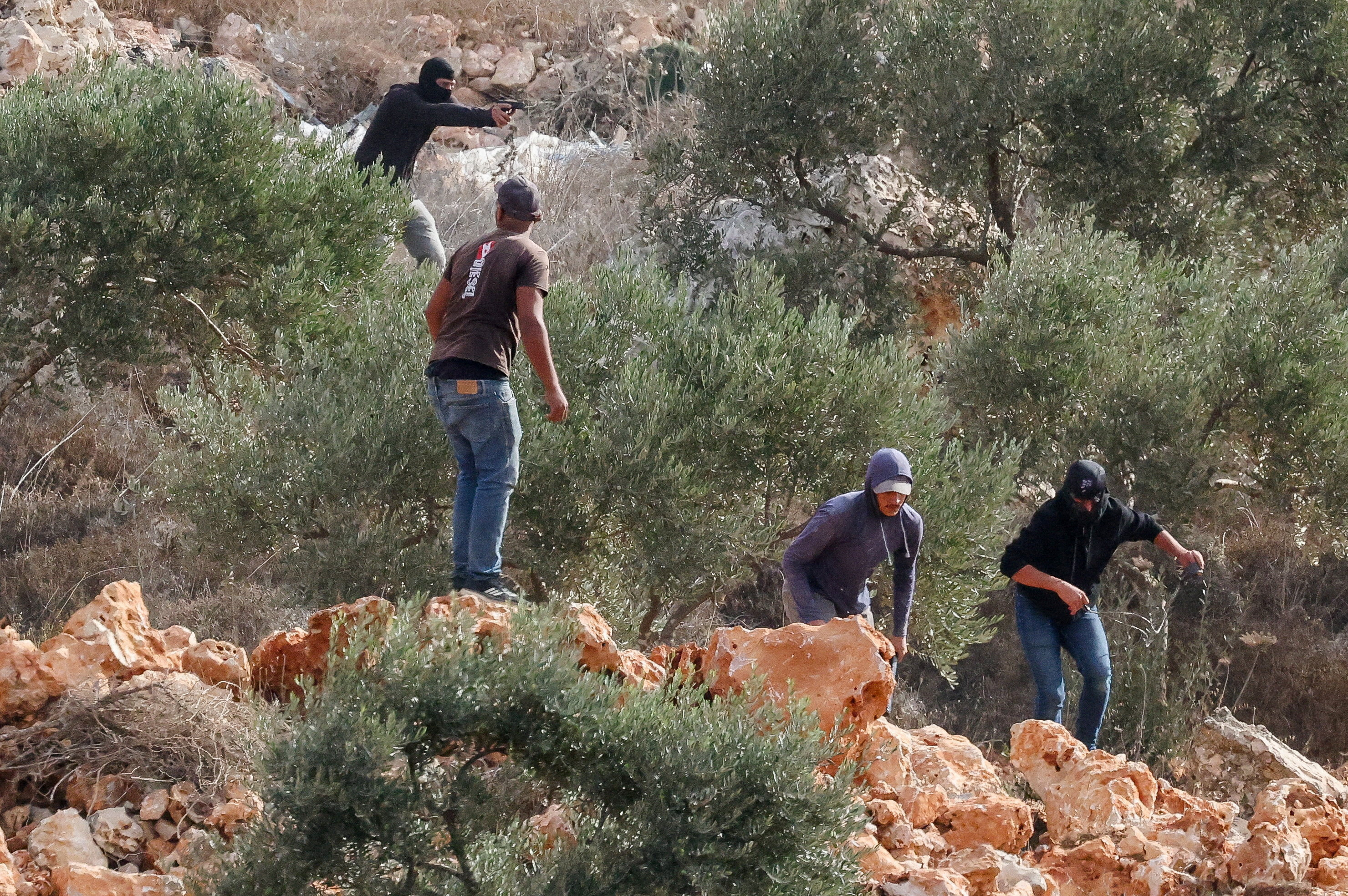 An Israeli settler points a gun amid clashes with Palestinians harvesting olives in Abu Falah near Ramallah in the Israeli-occupied West Bank, October 16, 2026. REUTERS/Ammar Awad     TPX IMAGES OF THE DAY