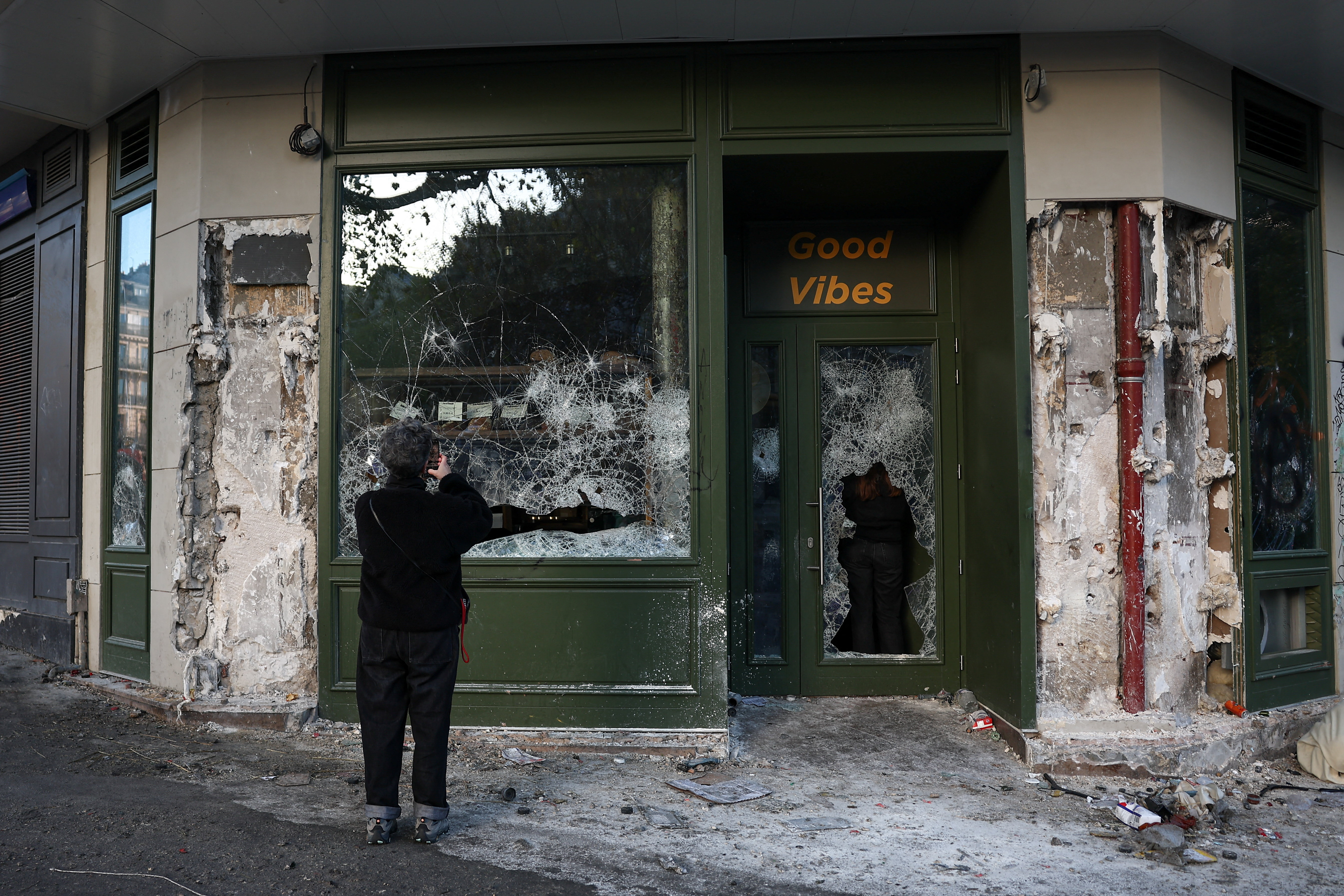 A person takes a photograph of a damaged shopfront, the day after clashes during a national day of demonstrations against the cost of living and rising fuel prices, near the Place de la Republique in Paris, France, October 18, 2026. REUTERS/Abdul Saboor