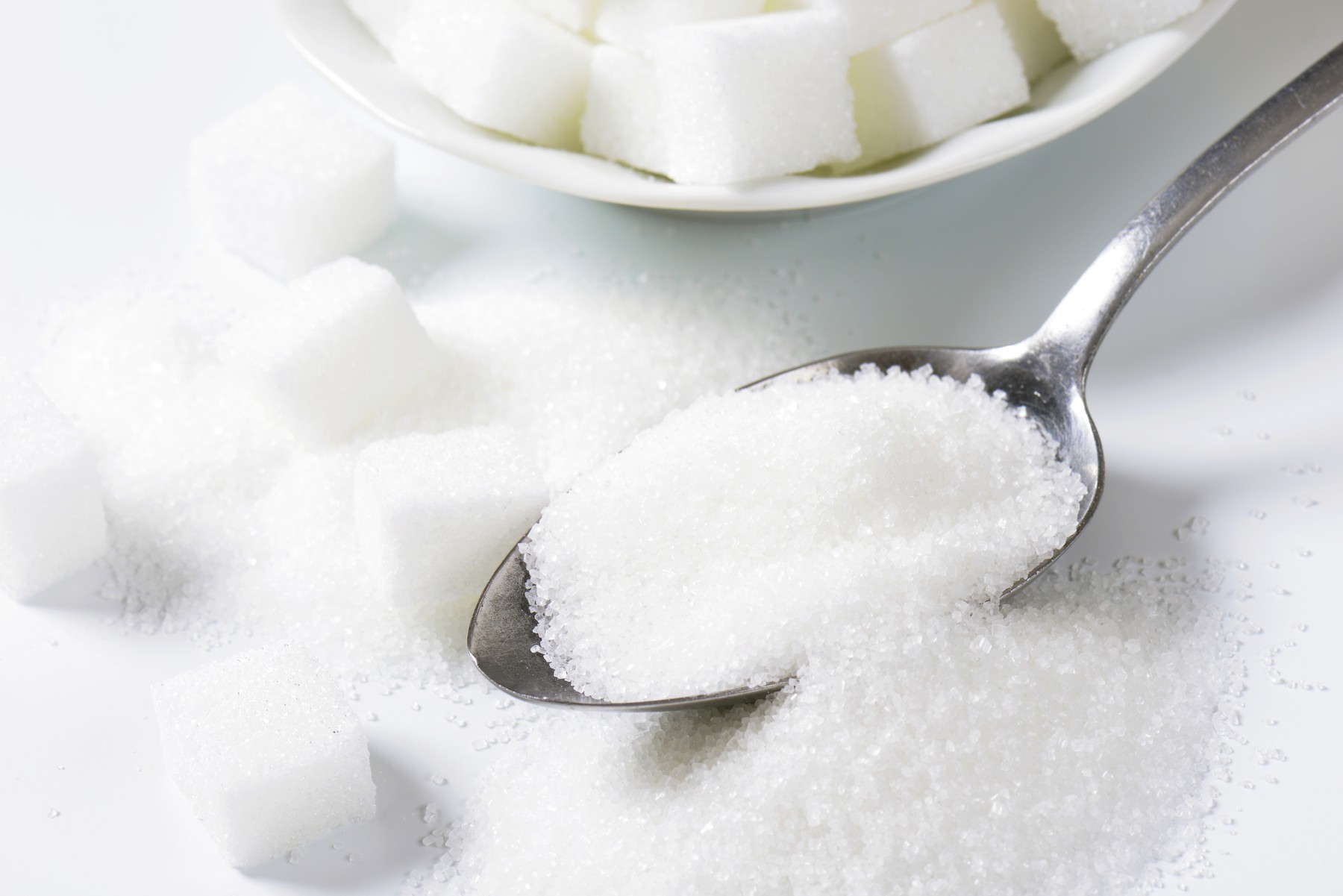 Spoonful of fine granulated sugar and pile of sugar cubes
