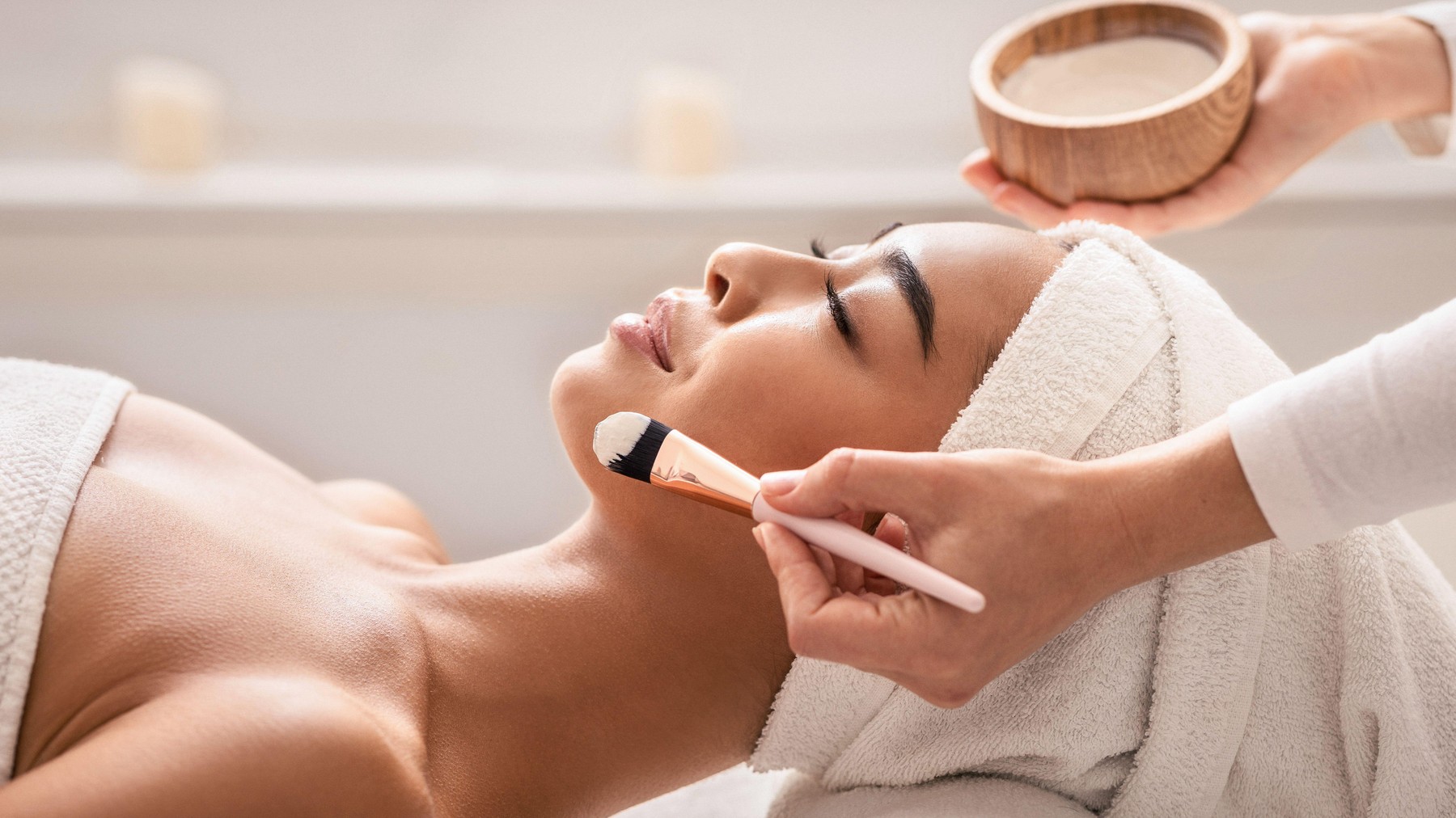 Beauty therapist applying face mask on young asian female skin at spa