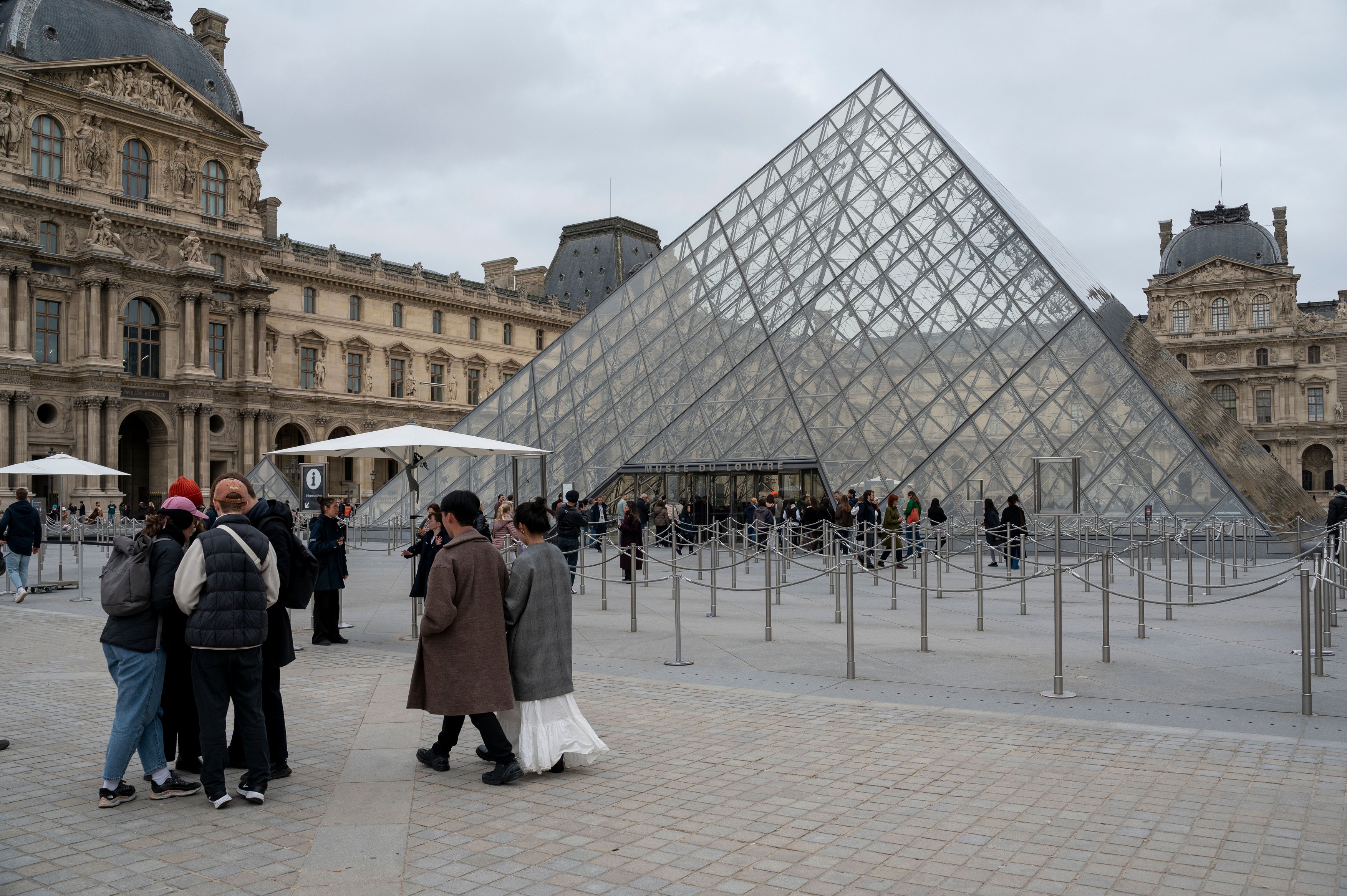 Tourists queue at the foot of the Louvre pyramid to visit the Louvre Museum,