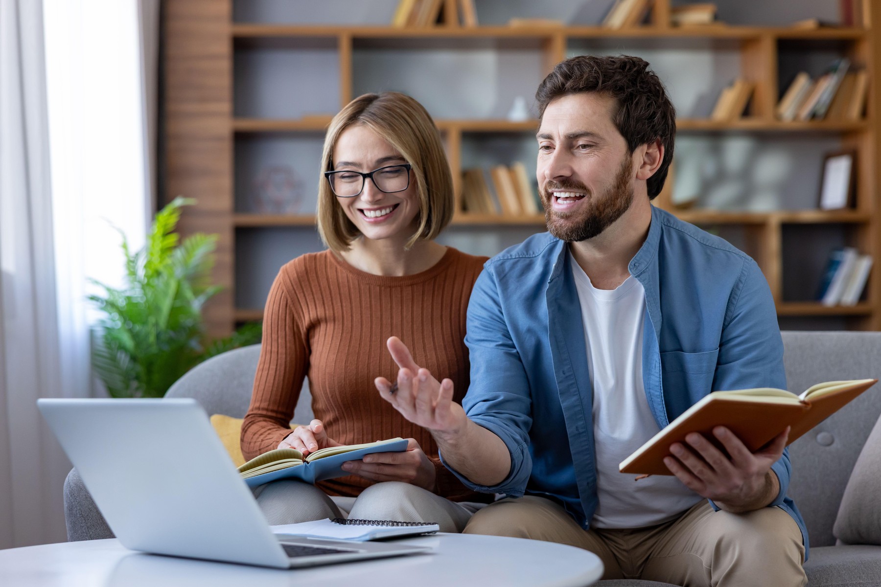 Happy couple studying together at home, smiling and discussing online course material while using a laptop and notebooks in a cozy living room workspace, focused and collaborative,Image: 1050439220, License: Royalty-free, Restrictions: , Model Release: no