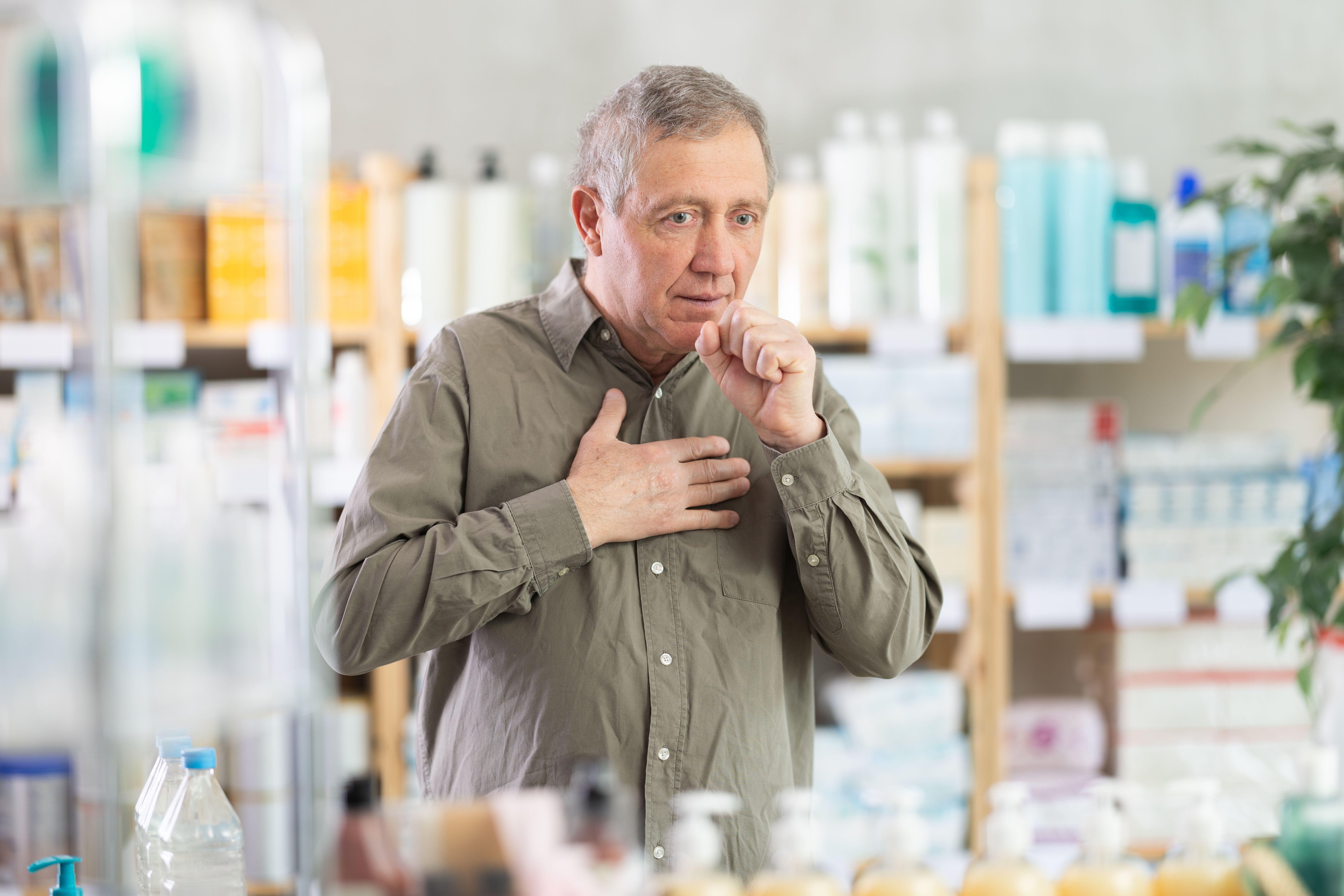Elderly man stands in a pharmacy with a cough and a sore throat, he is looking for medicines and syrups for a cold. Shopper at the pharmacy during the cold season,Image: 1010500485, License: Royalty-free, Restrictions: , Model Release: no