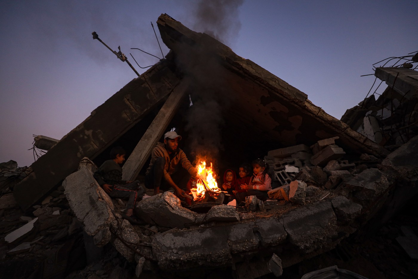 Otroci se grejejo ob ognju pod ruševinami v Džabaliji v Gazi