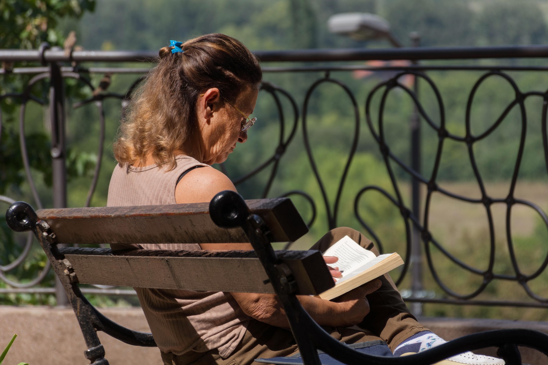 Niska Banja, Serbia - August 16, 2018: Senior woman on balcony sitting on bench and reading book on sunny summer day in spa resort. Recreation concept