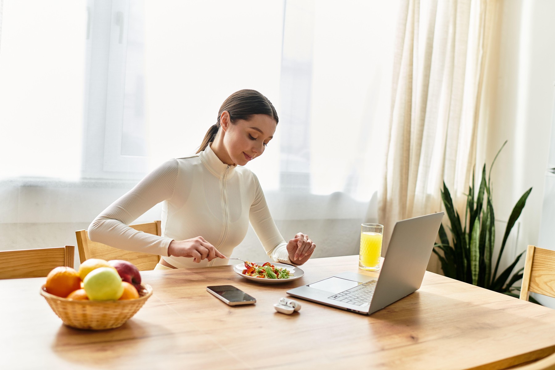 A young woman relishes a healthy breakfast of salad and juice at home, embracing wellness.