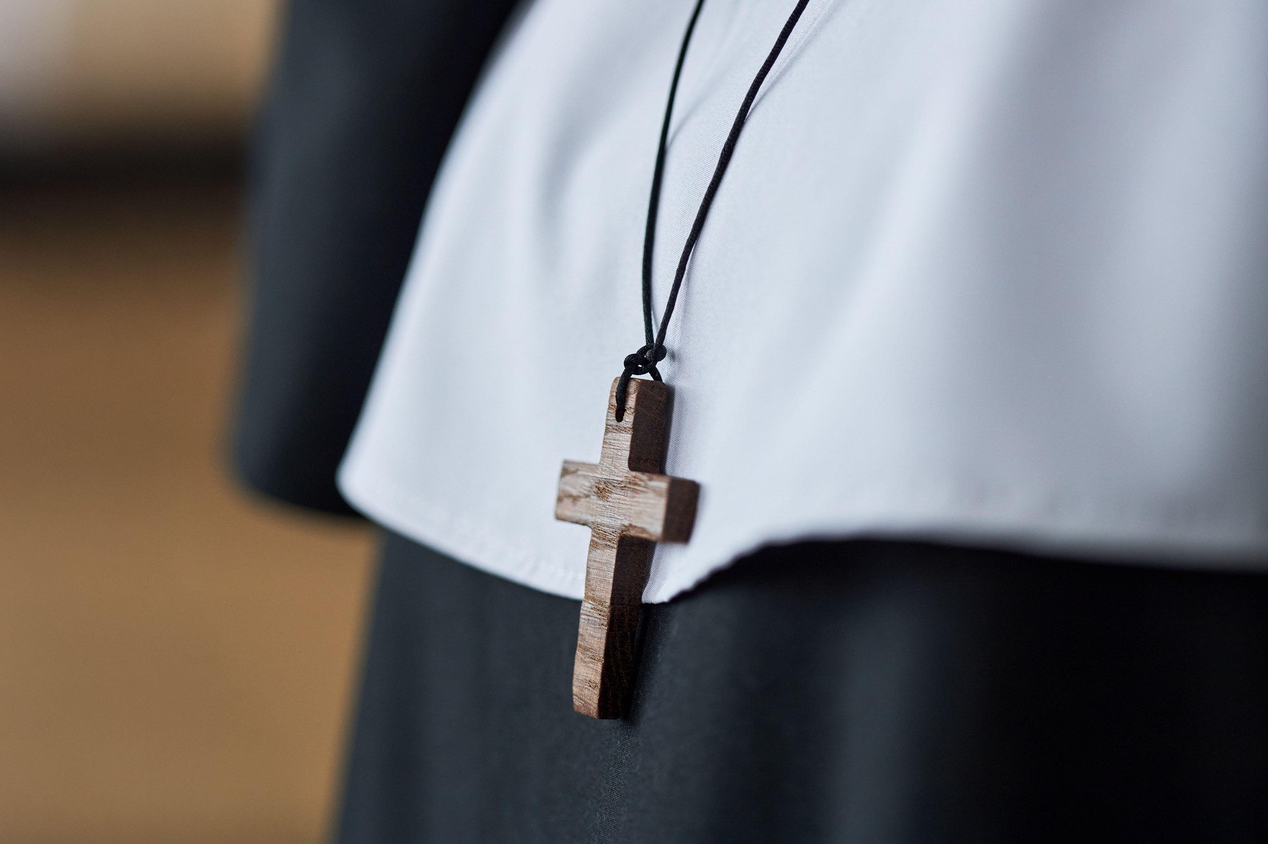 Close-up of wooden cross necklace hanging over a white garment, symbolizing faith and spirituality, worn by someone who could be in religious setting,Image: 996924970, License: Royalty-free, Restrictions: , Model Release: yes