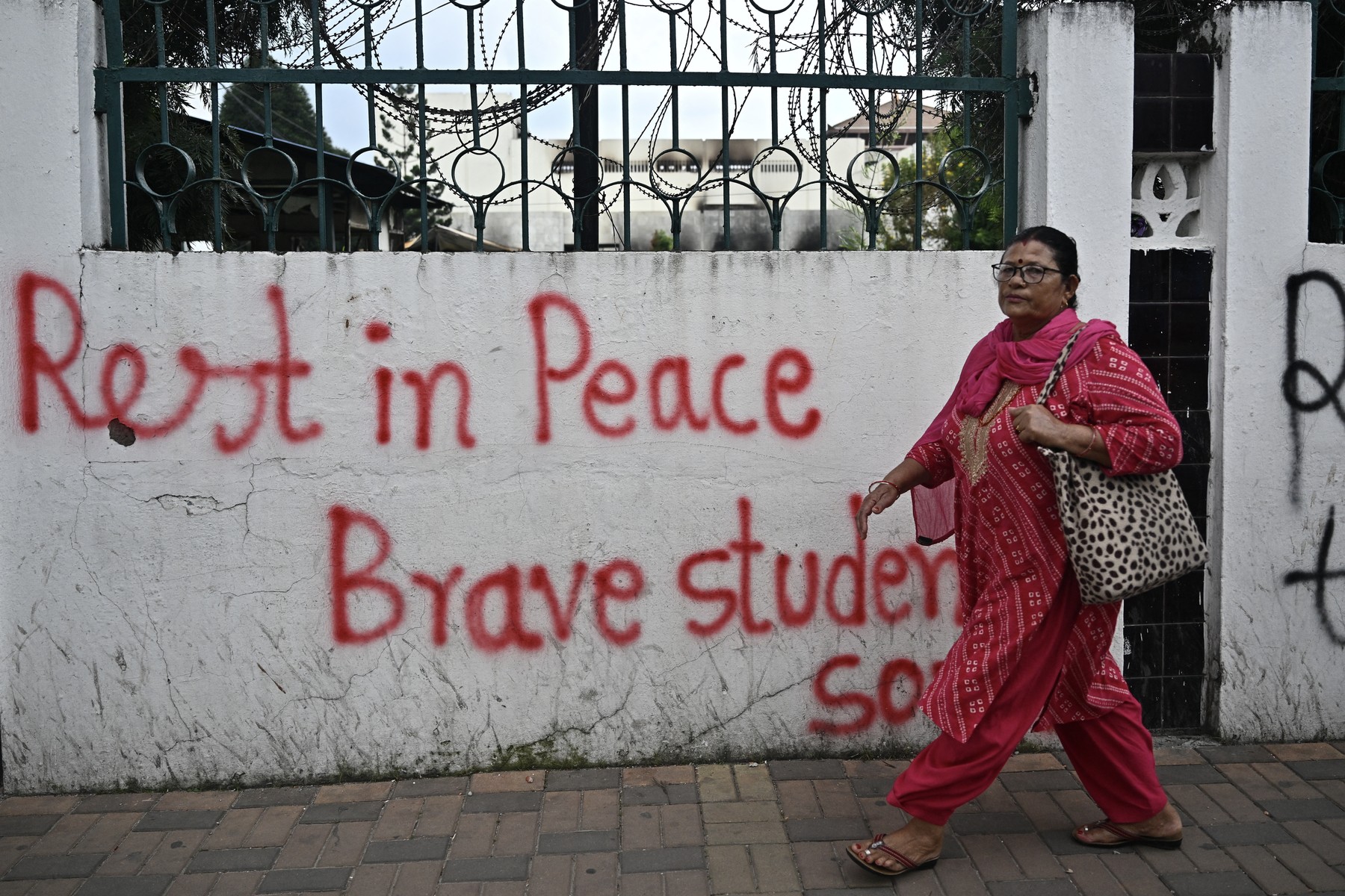A woman walks past a graffitied wall outside the torched Parliament building in Kathmandu