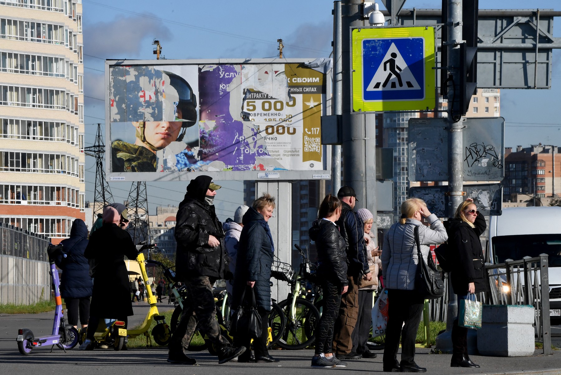 People wait to cross a street in front of a torn billboard promoting contract army service reading 'Join yours' in Saint Petersburg on October 10, 2023.,Image: 812592954, License: Rights-managed, Restrictions: , Model Release: no