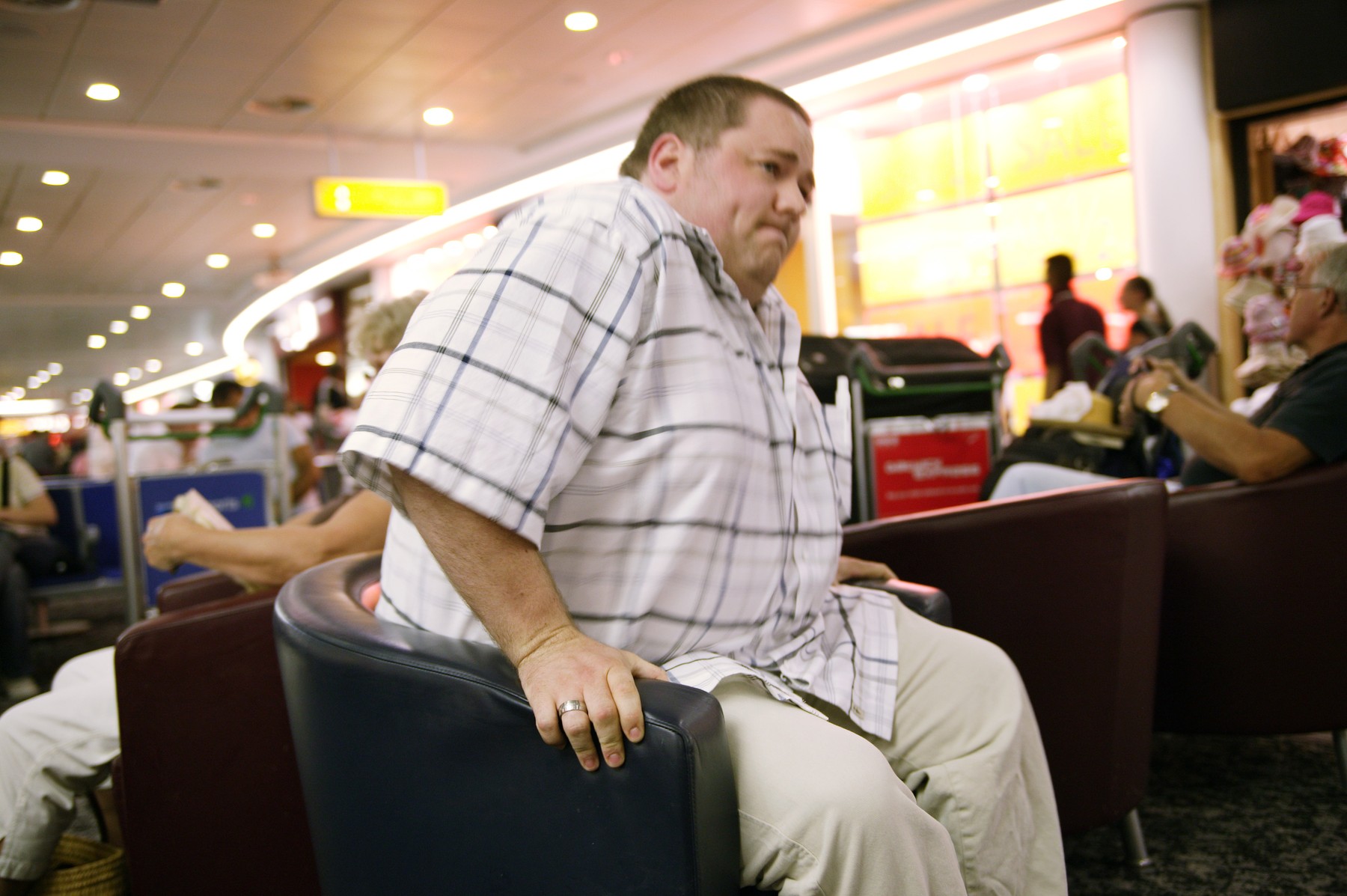 MODEL RELEASED. Obese man sitting down, while waiting for a flight at an airport.,Image: 102926196, License: Rights-managed, Restrictions: , Model Release: yes