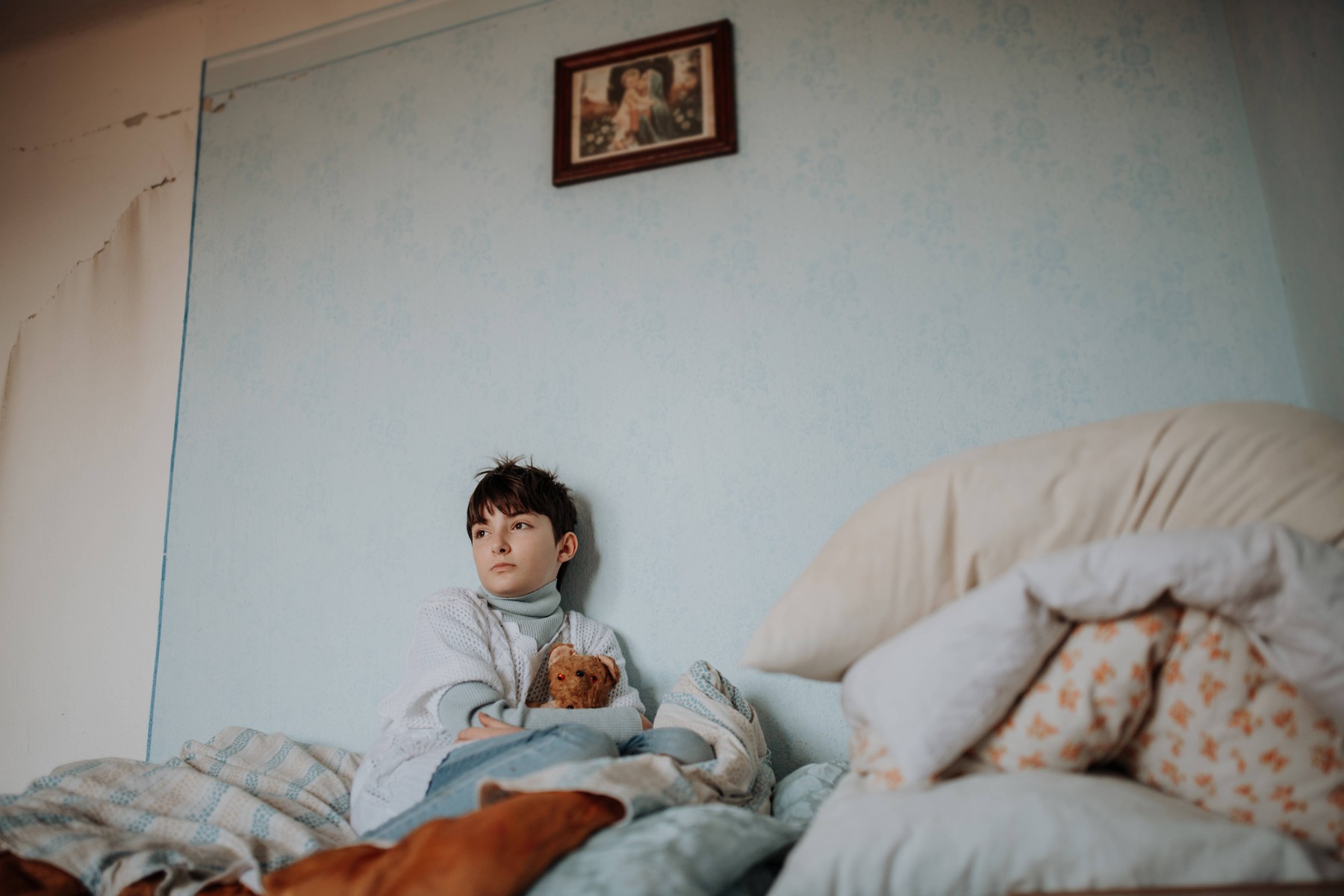 Sad orphan girl sitting alone in bedroom. Poverty concept.