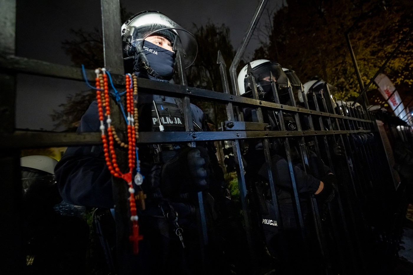 Police officers stand behind the fence with a rosary hanging on it as protesters