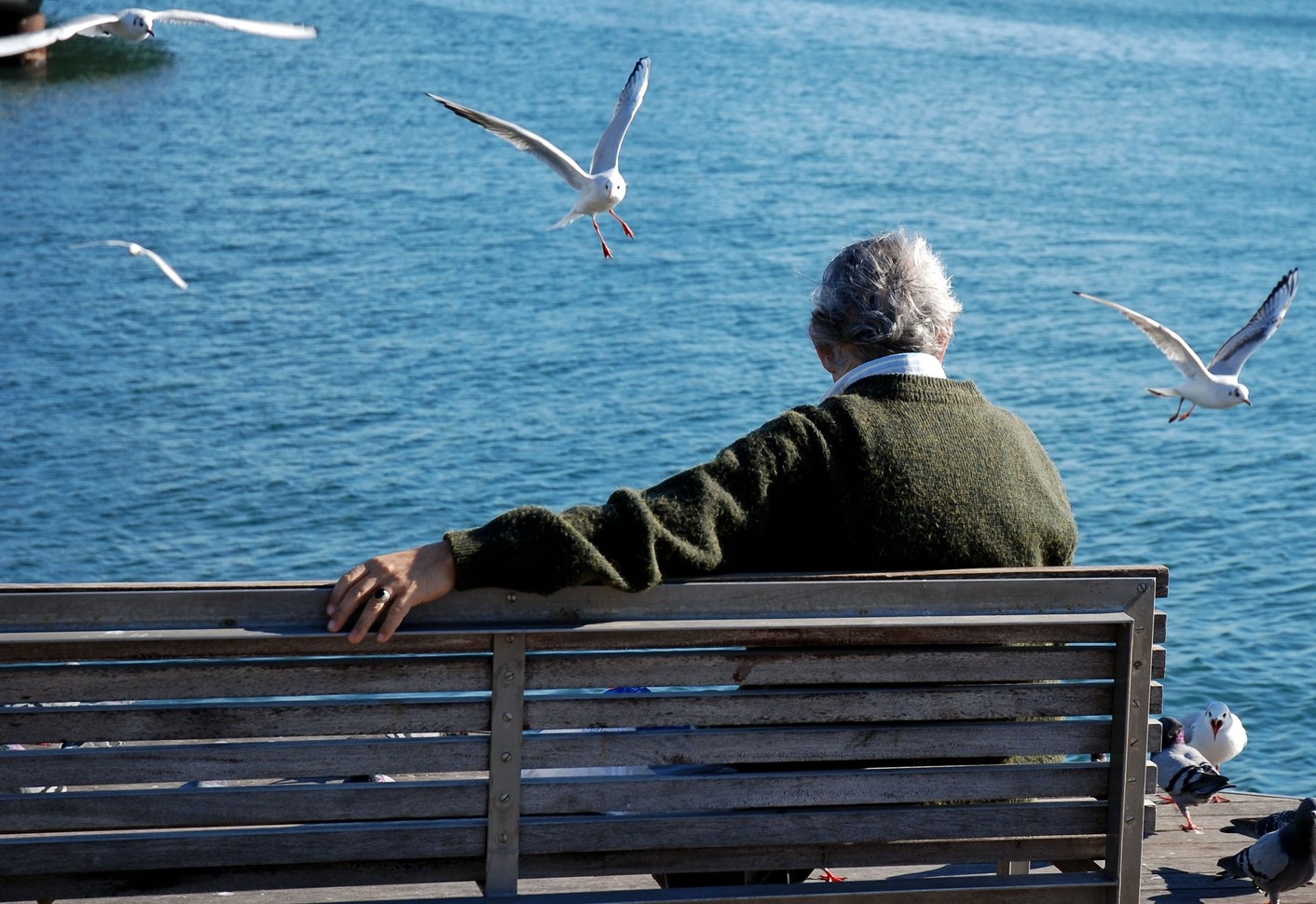 Starejši moški sedi na klopi ob morju.