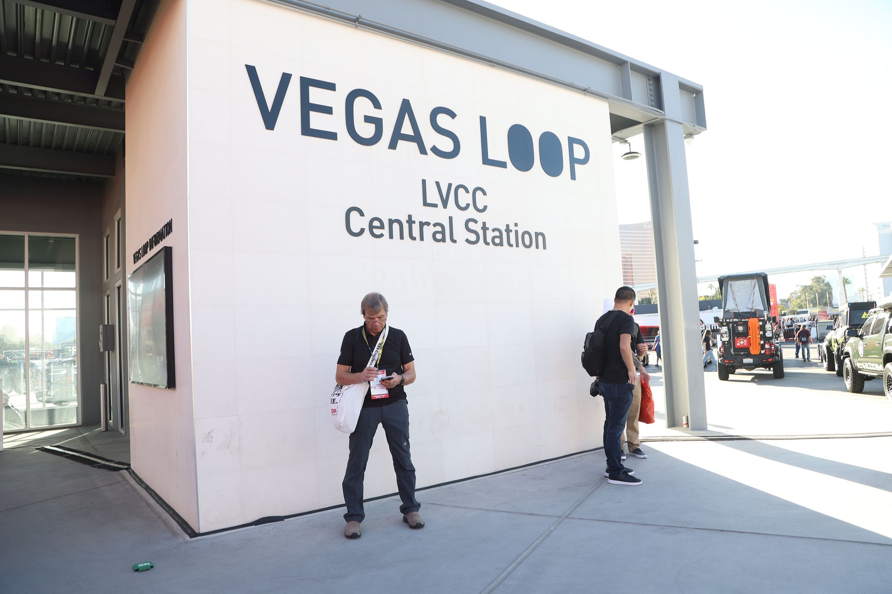 An attendee checks his smartphone while standing under a sign of a VEGAS LOOP s