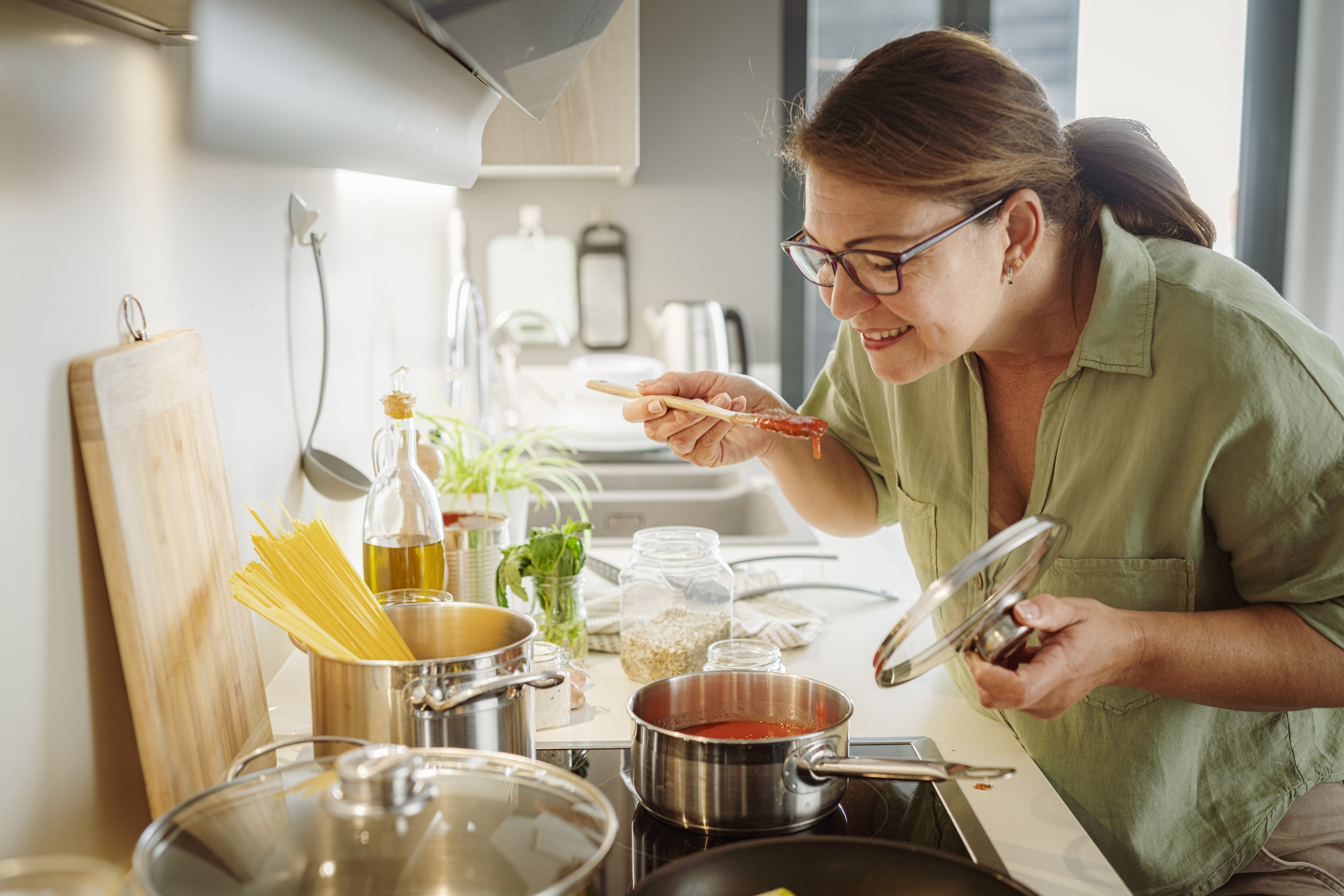 Smiling woman cooking spaghetti and tasting tomato sauce