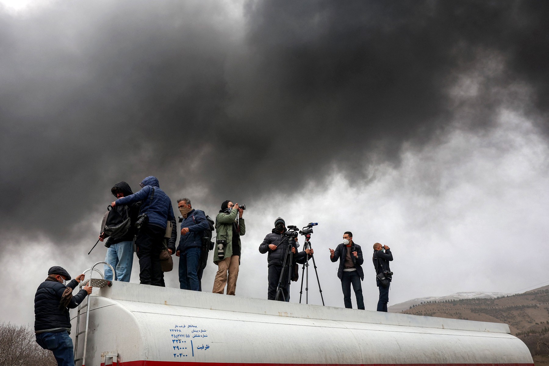 Journalists stand atop a fuel tanker as they cover a nearby ongoing fire following an overnight airstrike on the Shahran oil refinery in northwestern Tehran on March 8, 2026.